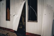 Damaged white trailer wall with torn siding and broken window after severe storm damage