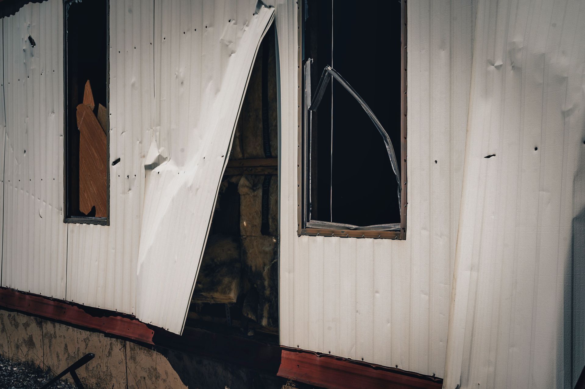 Damaged white building with a torn-open wall and shattered window.