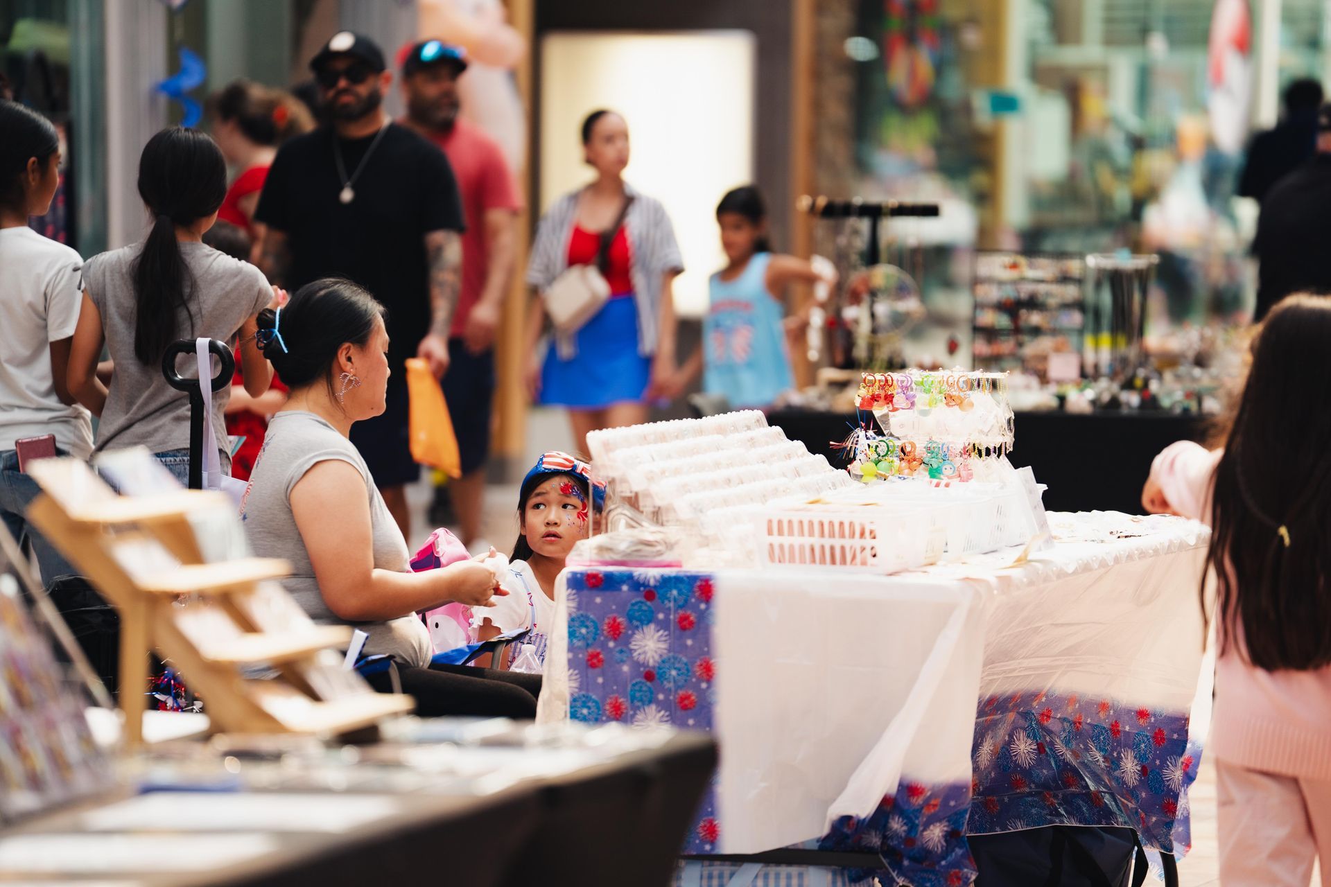 People seated at an outdoor market table near colorful goods and pedestrians
