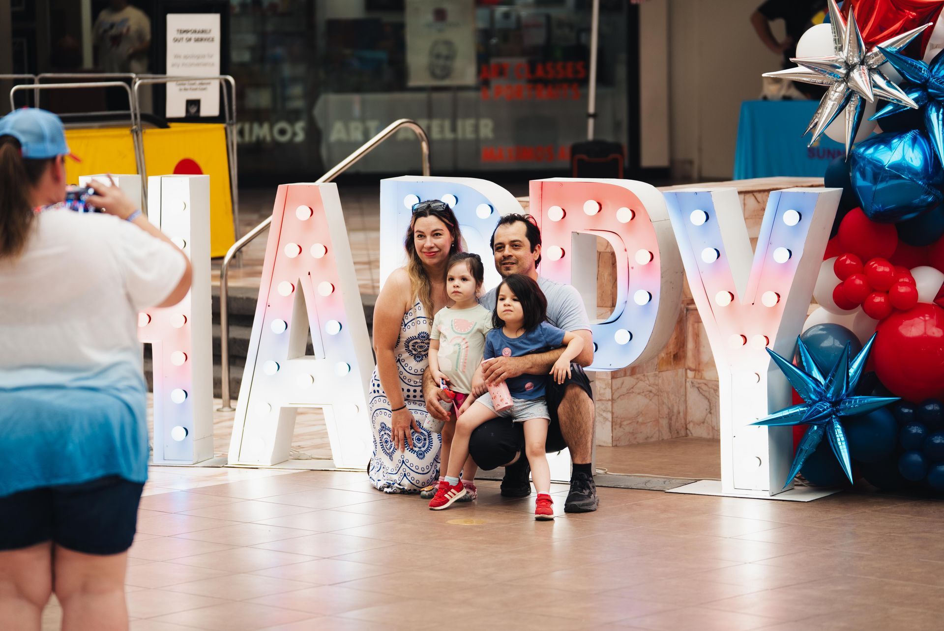 Family posing in front of large lit letters and balloons at a mall celebration event