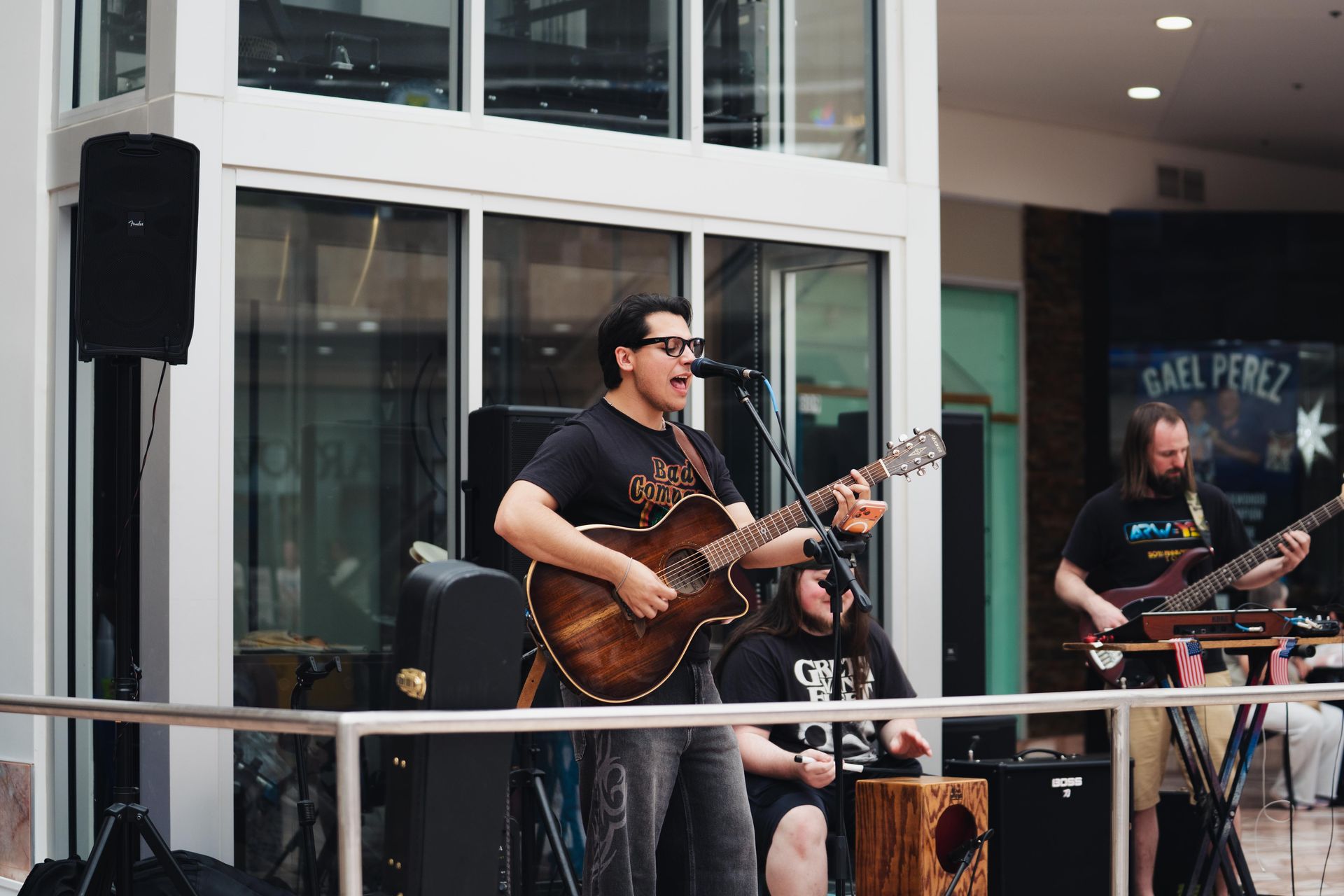 Musicians performing live on an outdoor patio, with a singer-guitarist at a microphone and a drummer nearby
