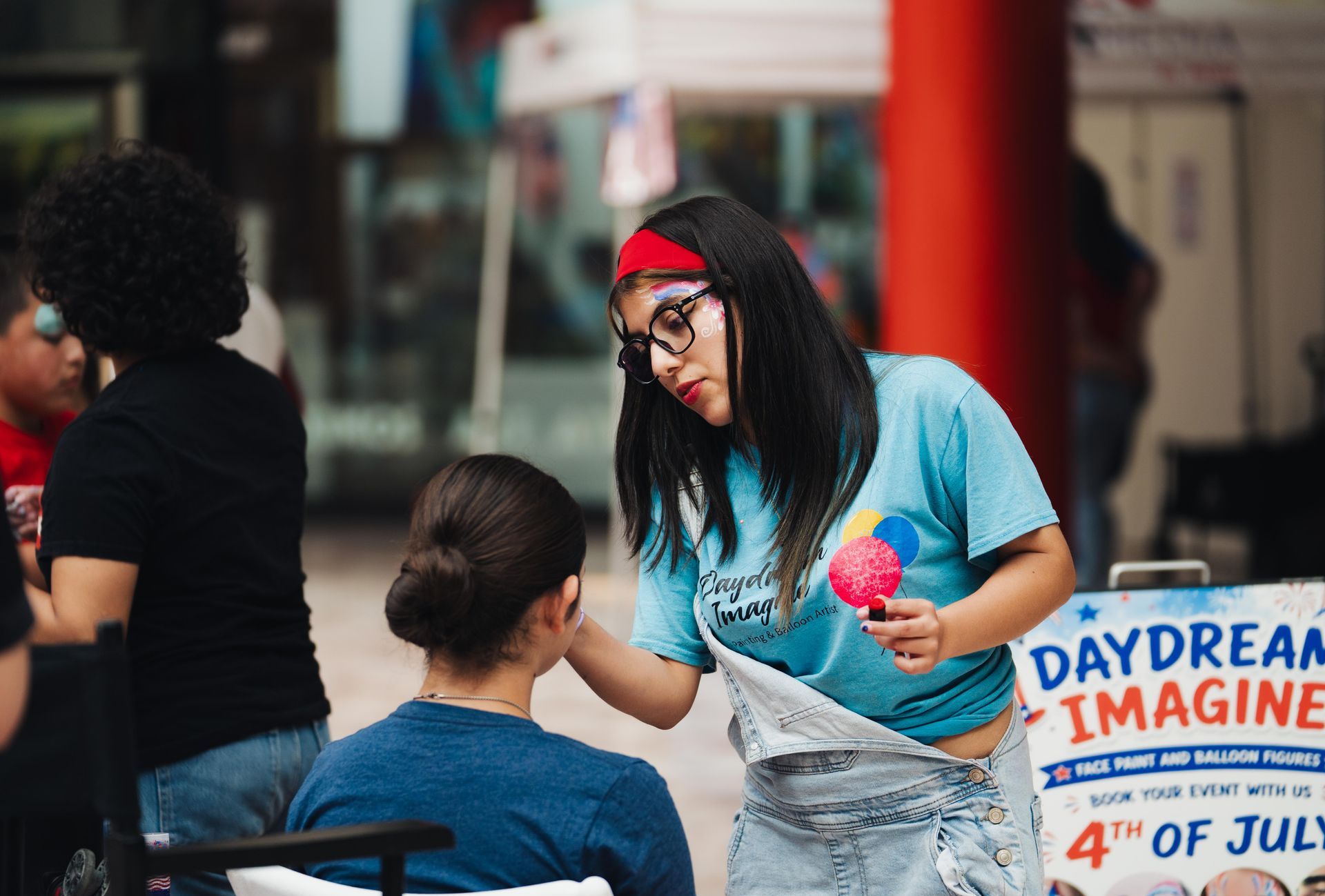 Woman in blue shirt handing an item to a seated person at a community event booth with a Daydream sign