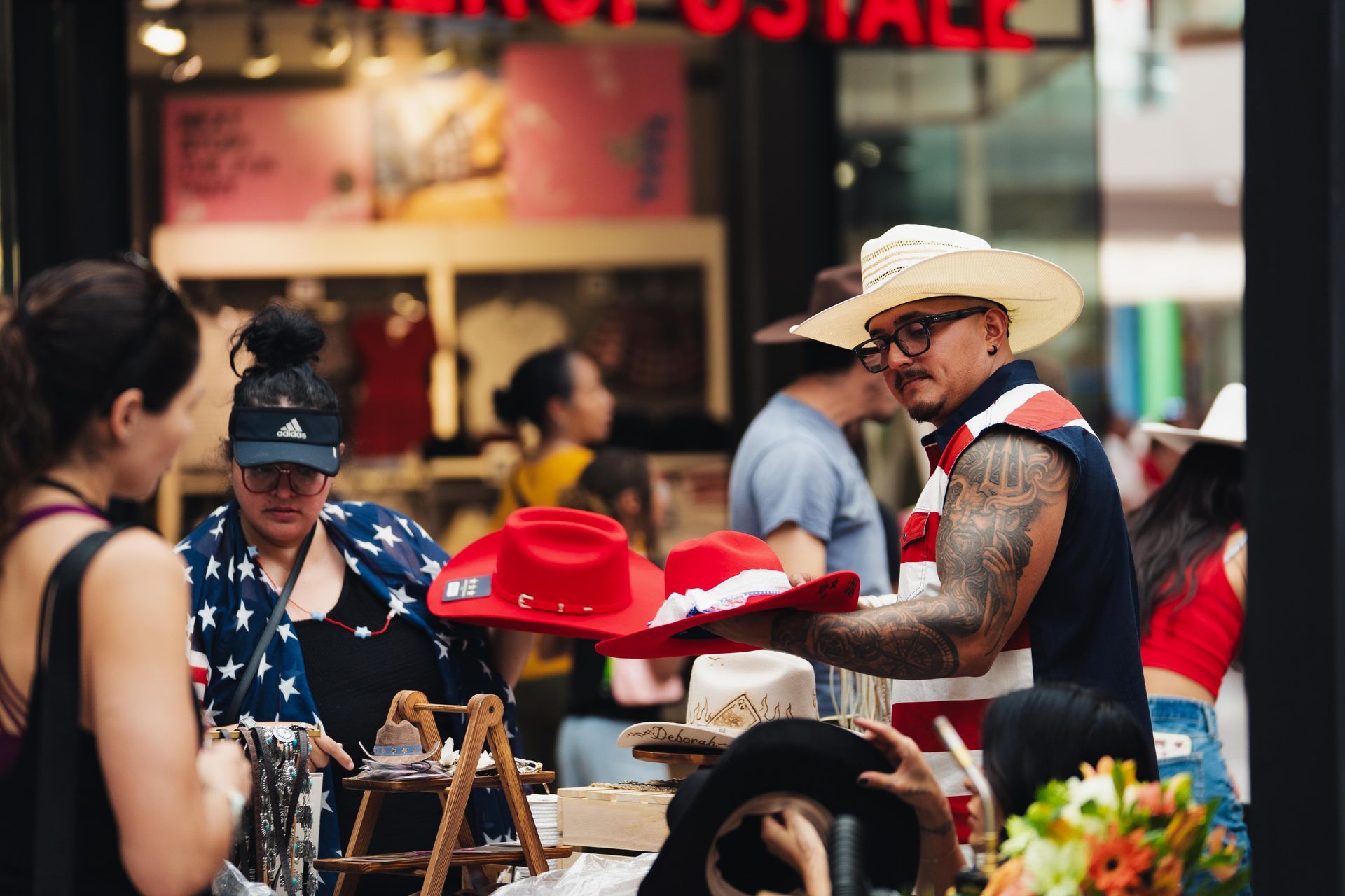 People browsing hats at an outdoor market stall, with colorful red and black hats on display
