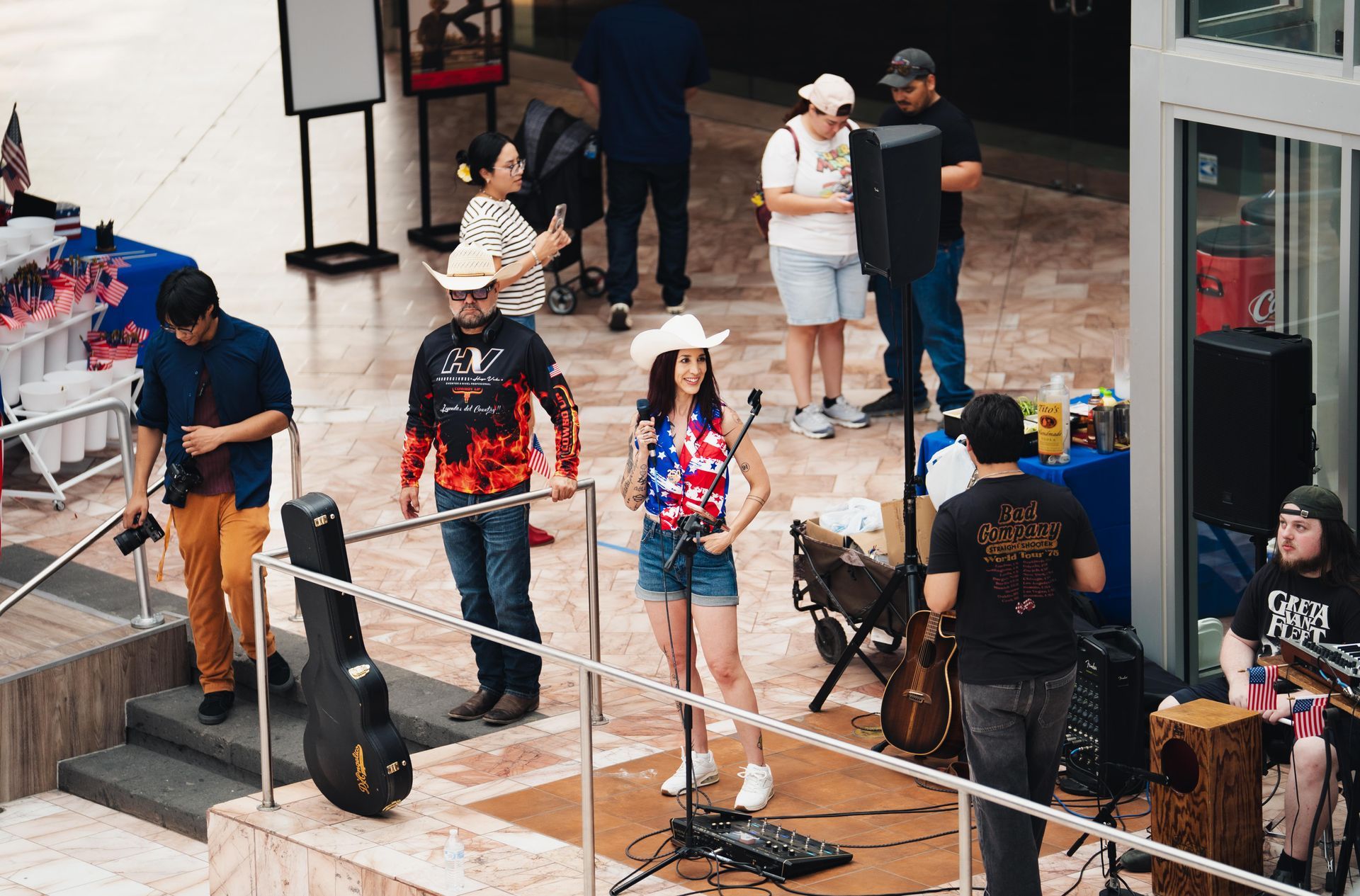 Outdoor street performance with musicians on a small stage, including a singer, guitarist, and drummer