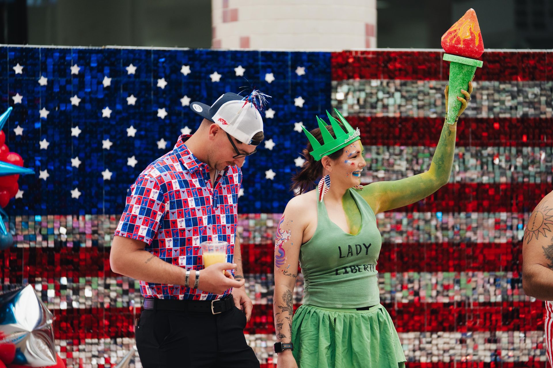 People in patriotic outfits celebrating in front of an American flag backdrop
