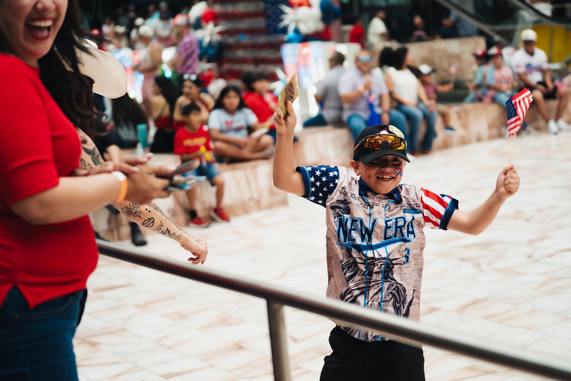 Child in patriotic shirt holding small American flags at a crowded outdoor event