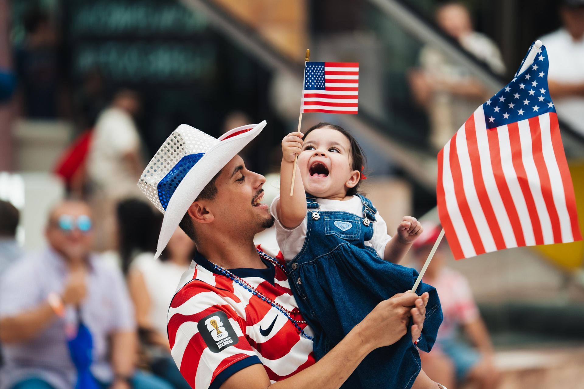 Person holding a child with small American flags at a festive outdoor event