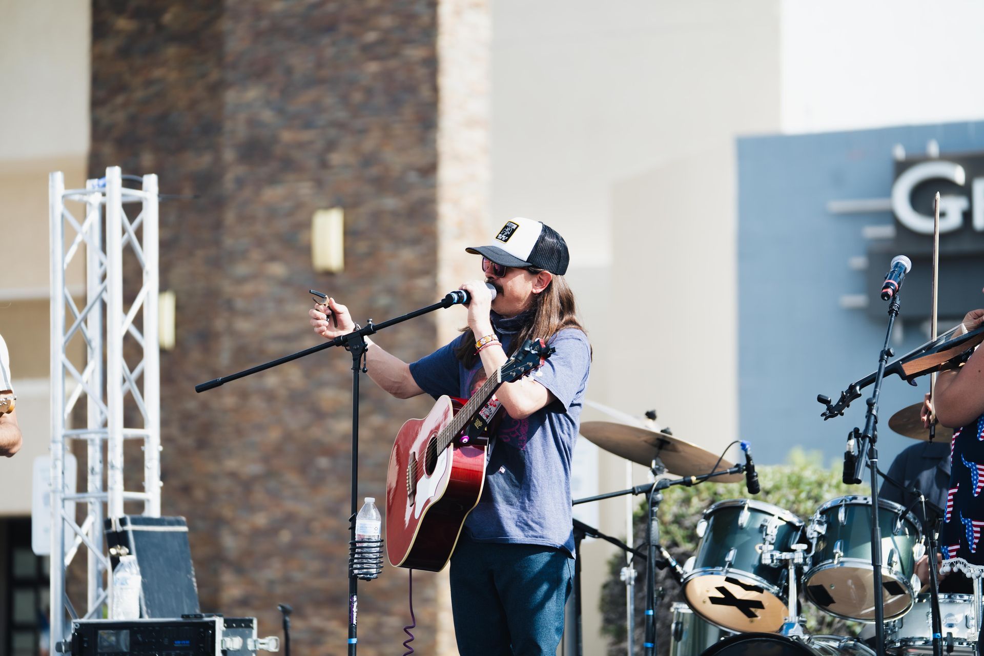 Musician singing and playing guitar on an outdoor stage with drums behind him