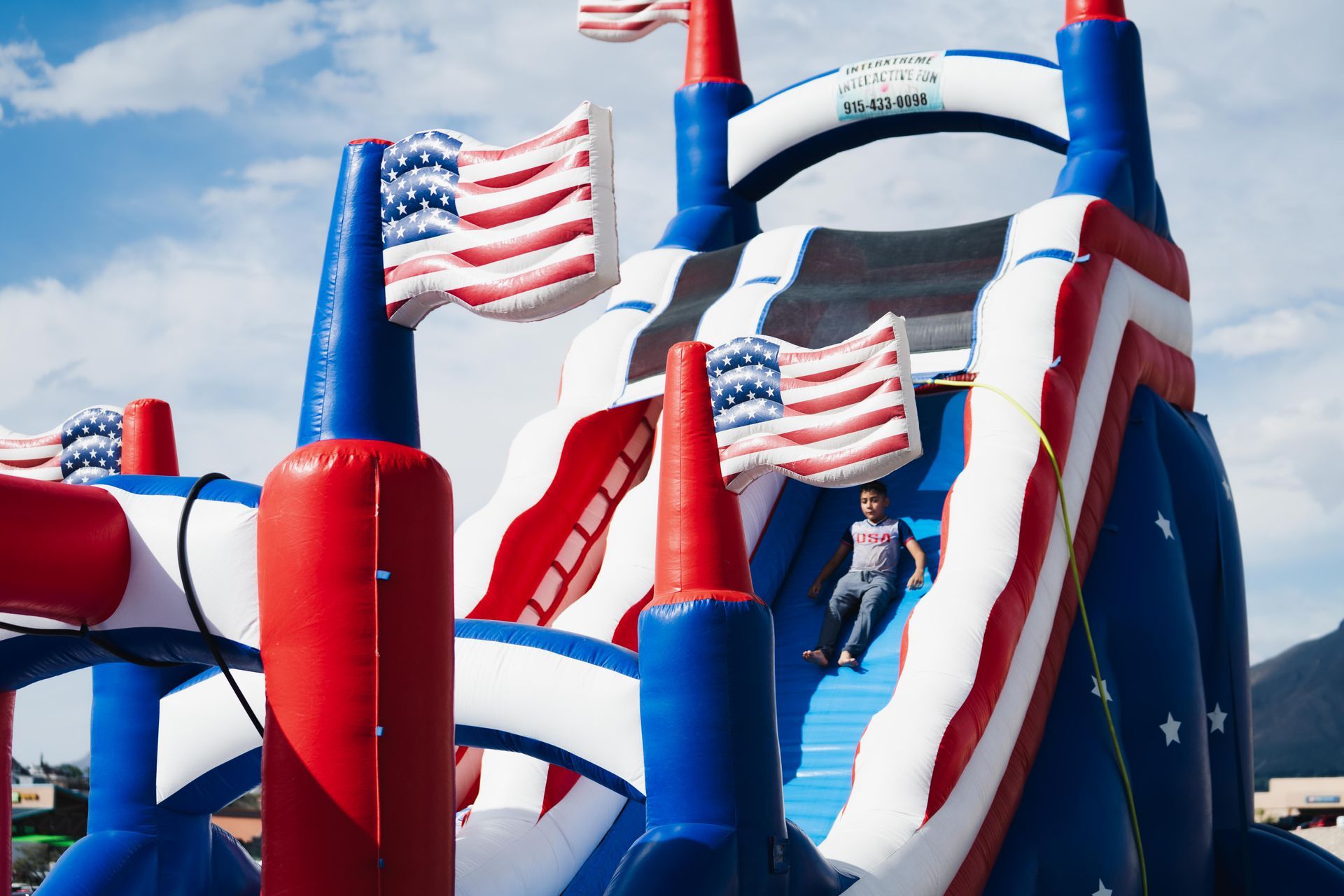 Red, white, and blue inflatable obstacle course with American flags and a child climbing inside