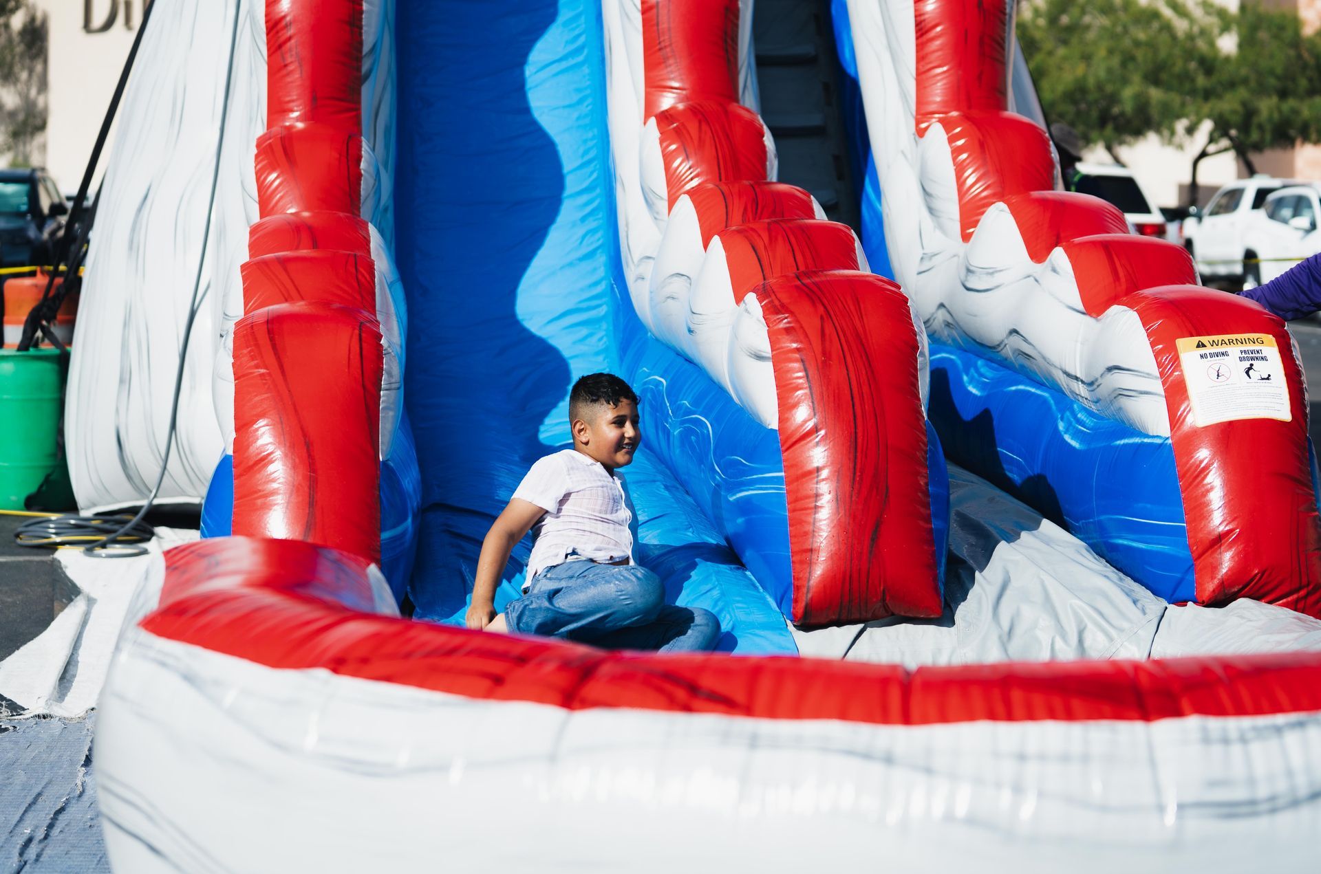 Child sitting at the base of a red, white, and blue inflatable slide