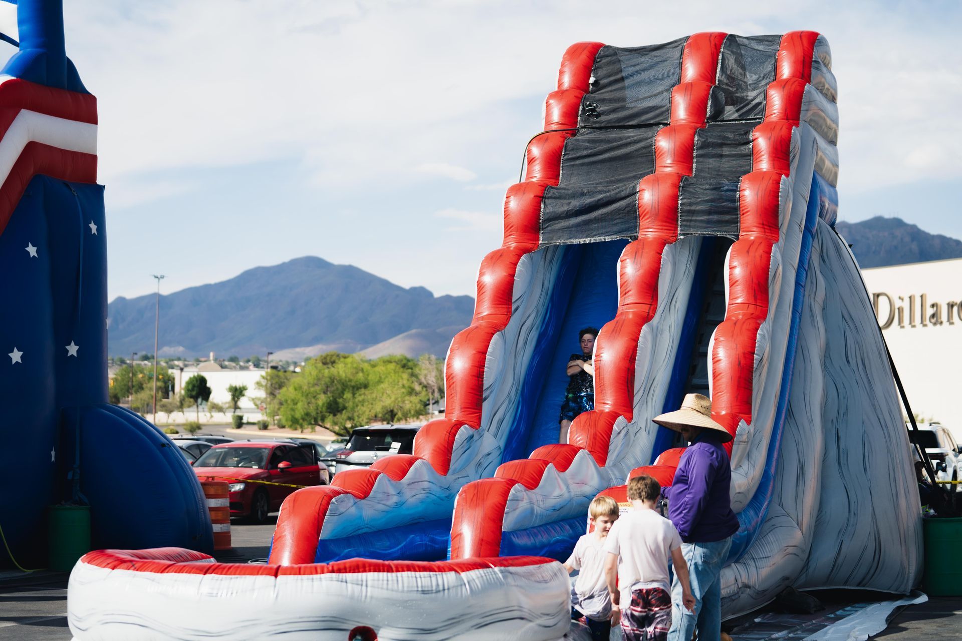 Inflatable red, white, and blue slide at an outdoor event with mountains in the background