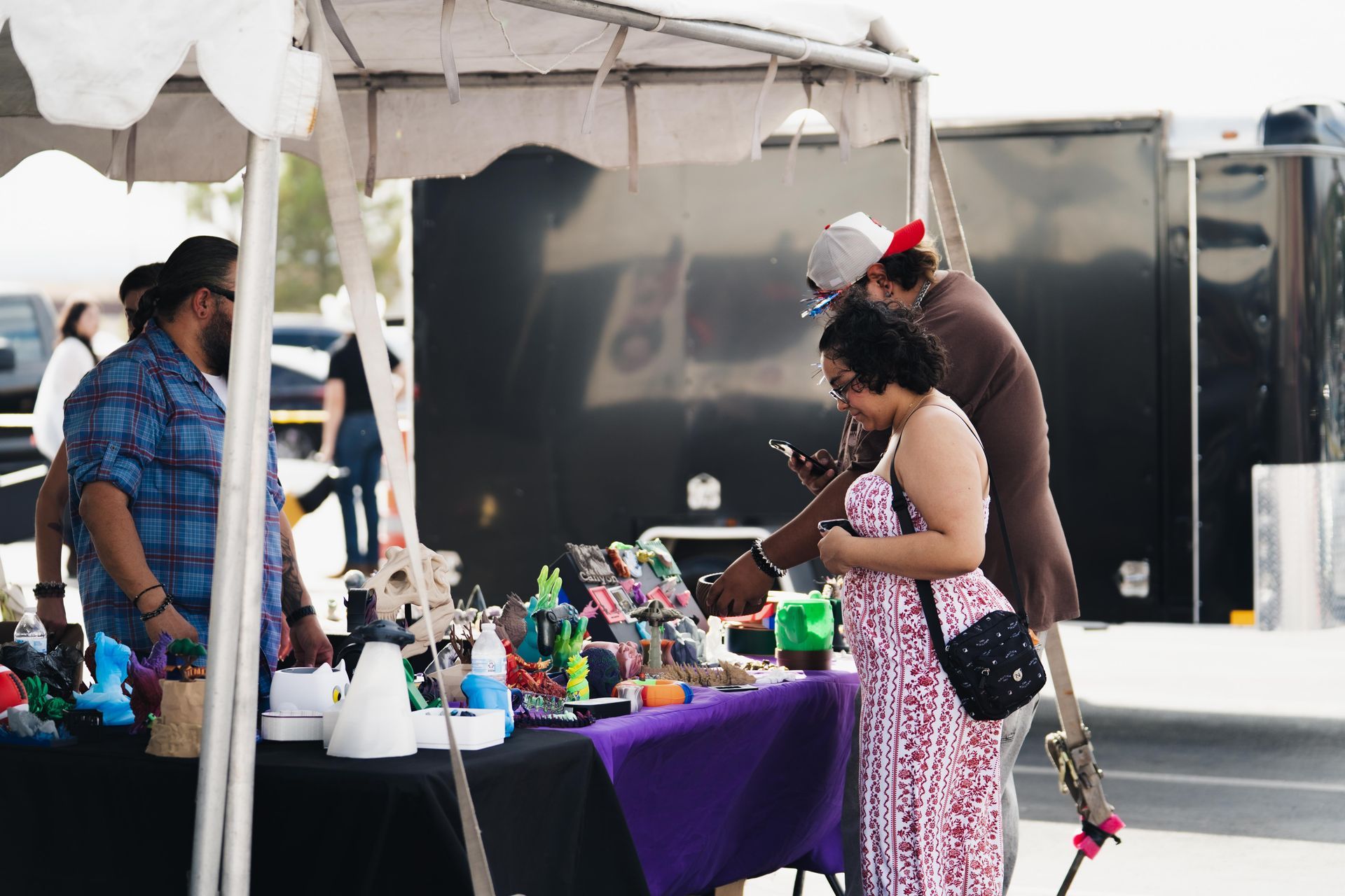 People browsing colorful handmade goods at an outdoor market stall under a white tent