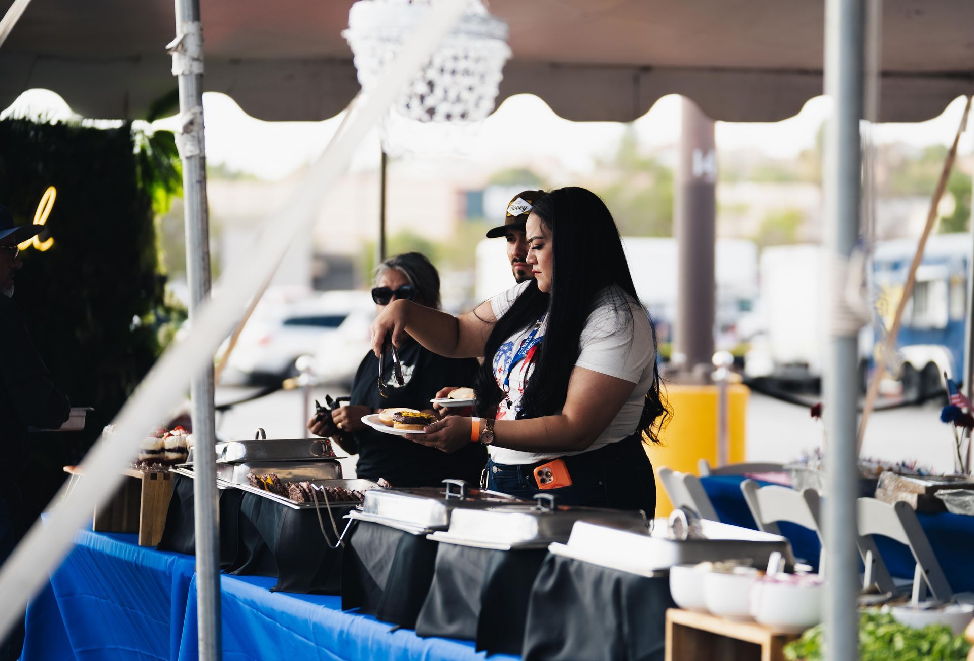 Two people cooking at an outdoor market stall under a white canopy, with pans and serving trays on the counter.