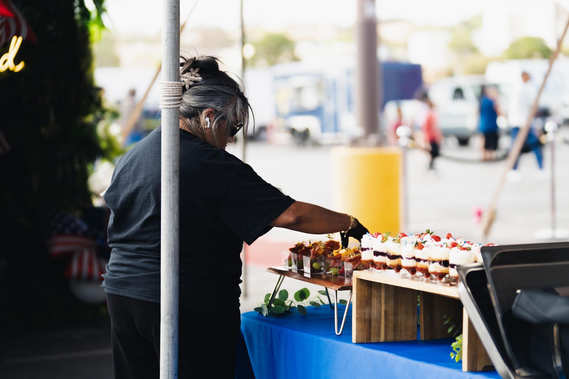 Person reaching for items at a street market stall with blue tablecloth and potted flowers