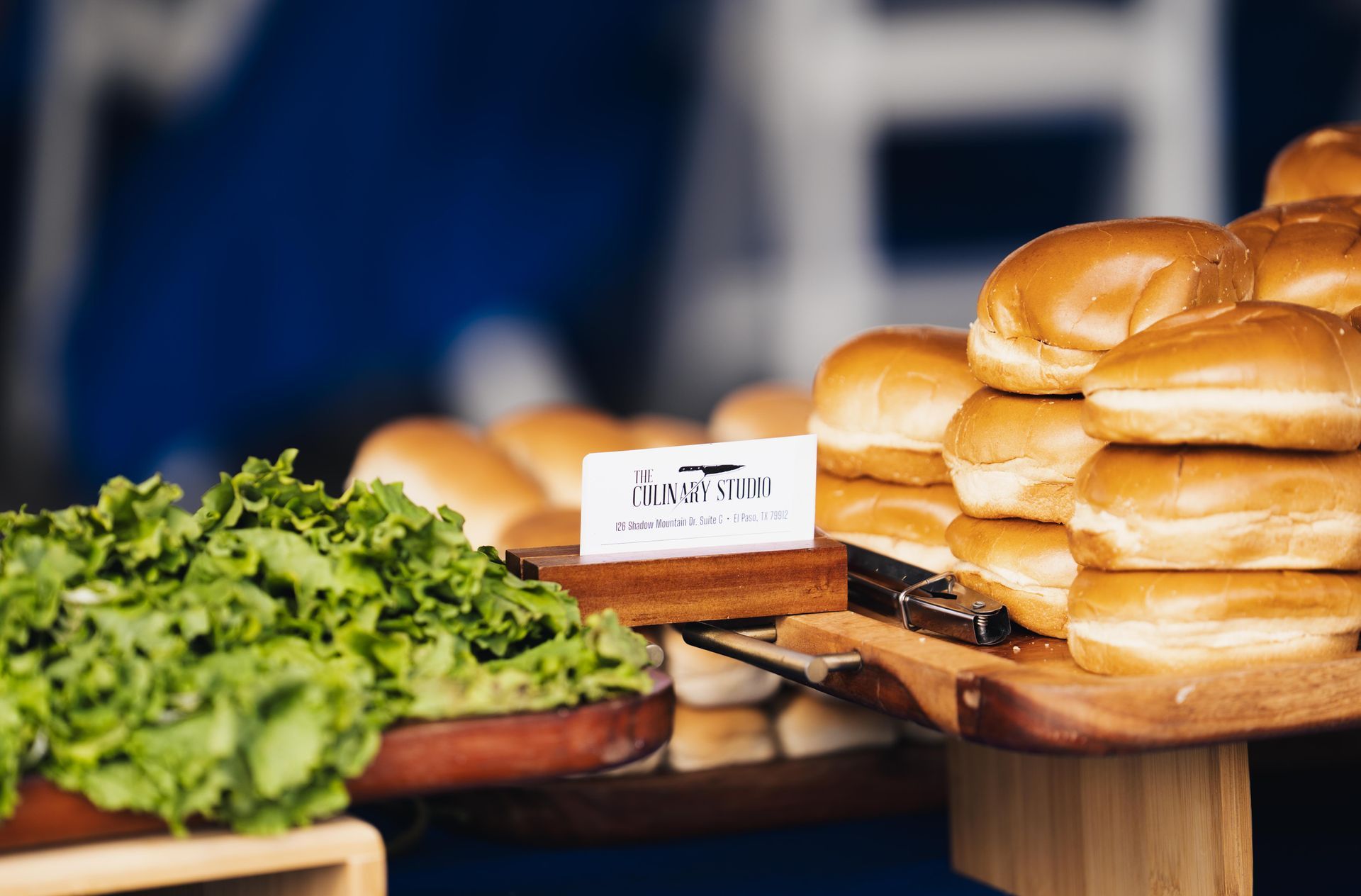 Assorted bread rolls on wooden stands beside leafy greens at a buffet display.