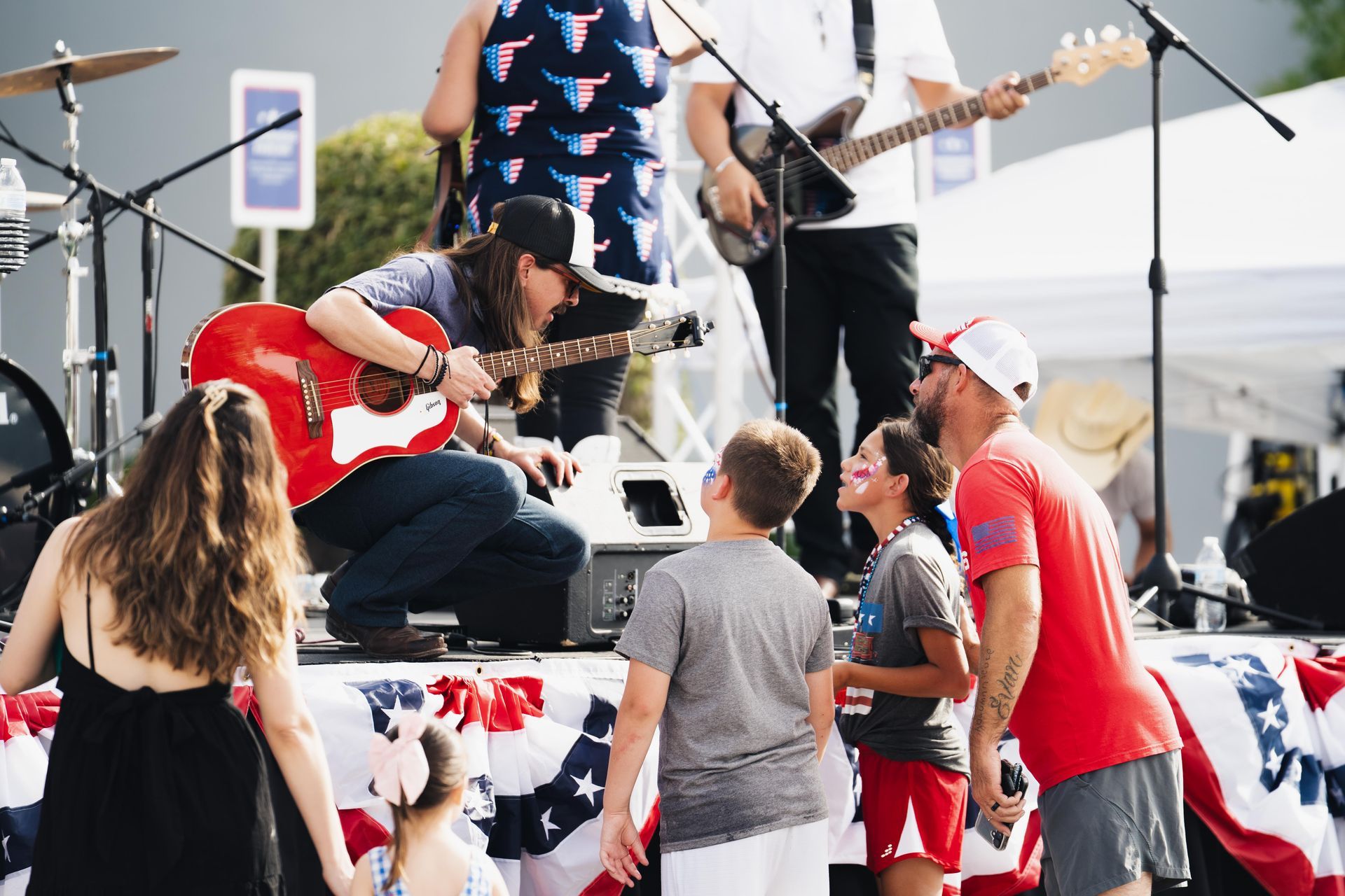 Live band performing on an outdoor stage with audience members watching nearby