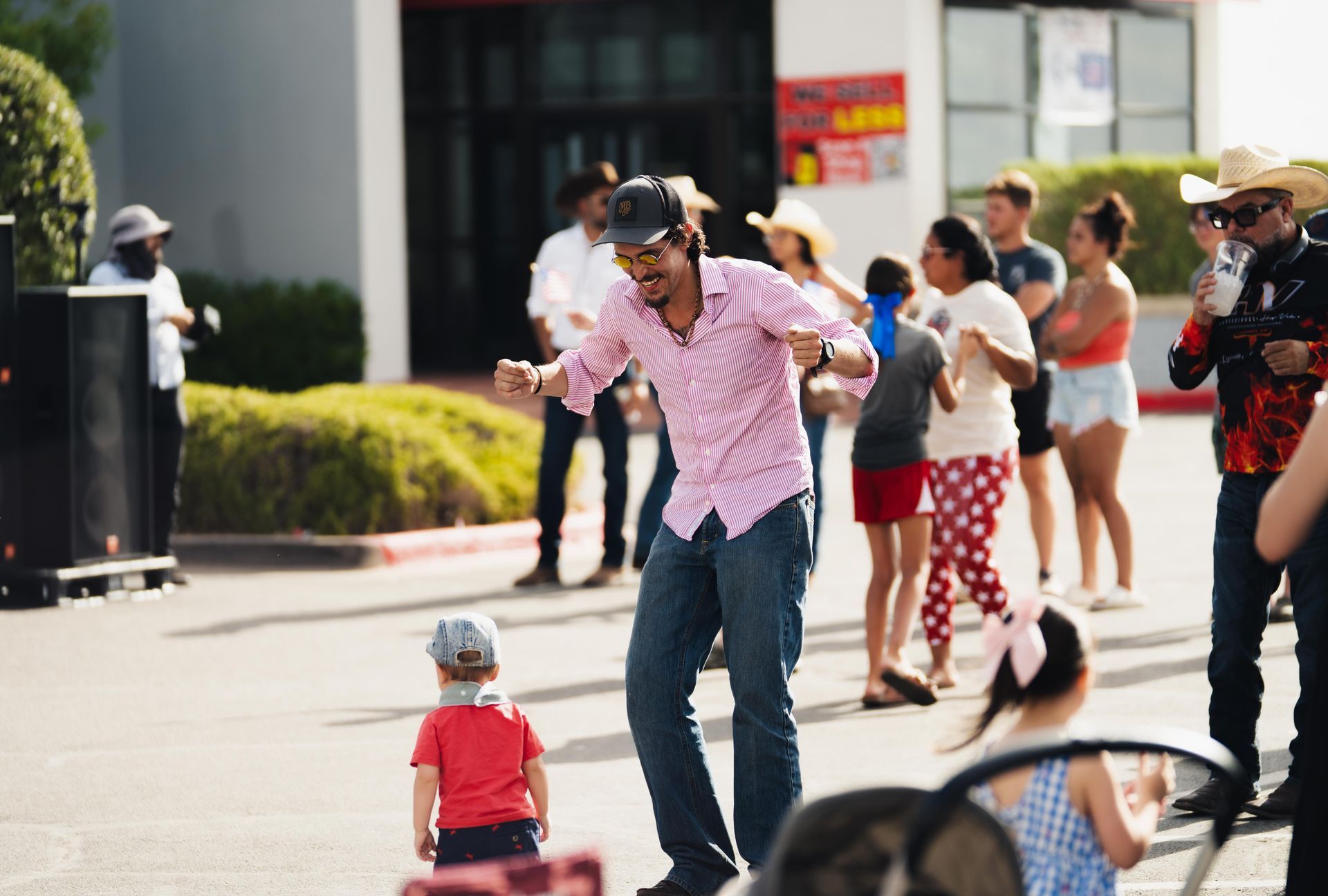 Dancer in a pink striped shirt performs outdoors while a small child watches nearby.
