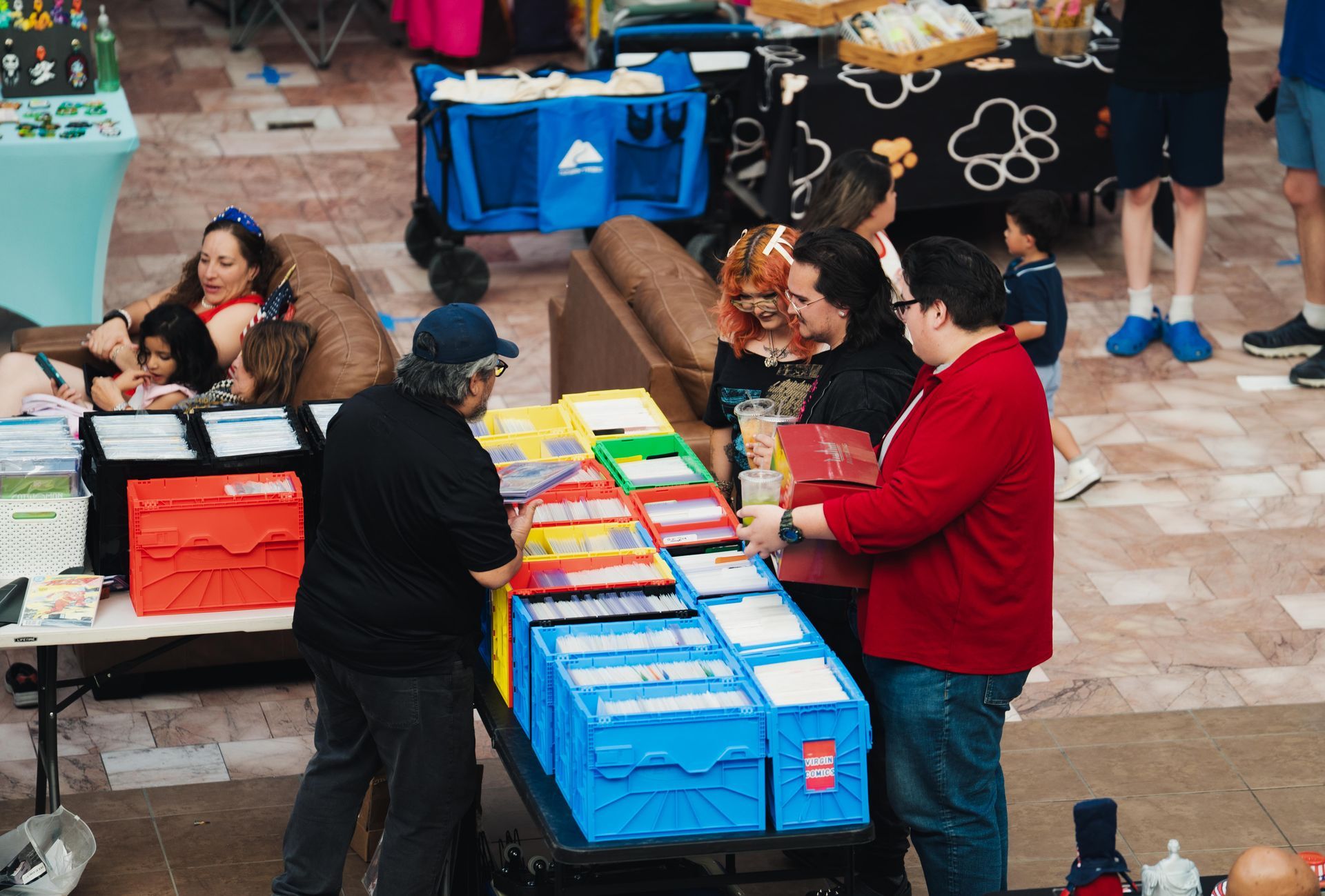 People sorting colorful stacked bins and boxes at an outdoor market stall