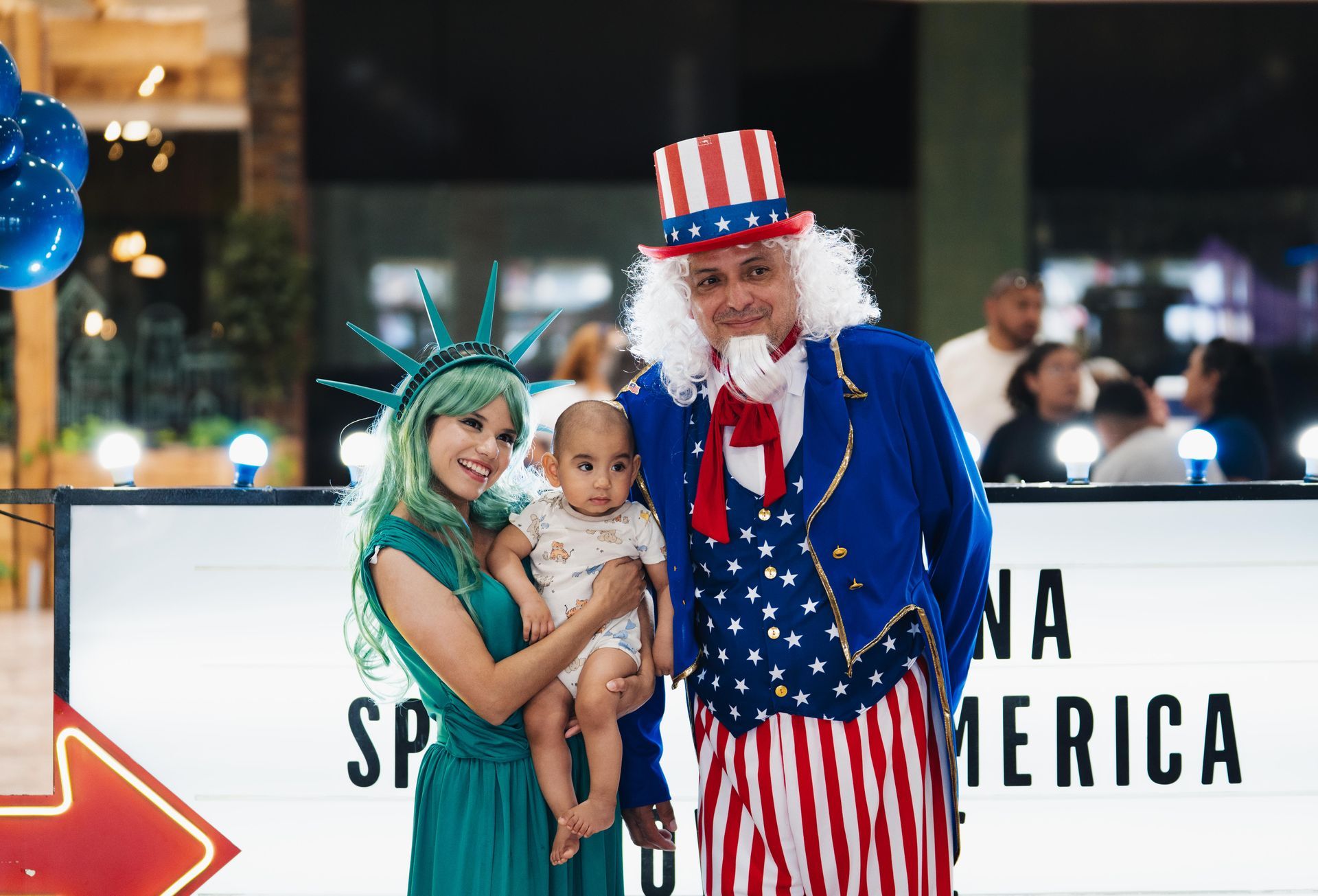 Costumed performers posing with a child in front of a “Spend America” sign at an indoor event