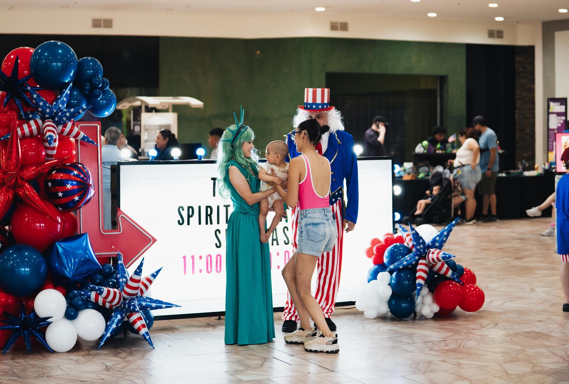 People at a patriotic-themed event booth with red, white, and blue balloons and a sign reading “Spring Fling”