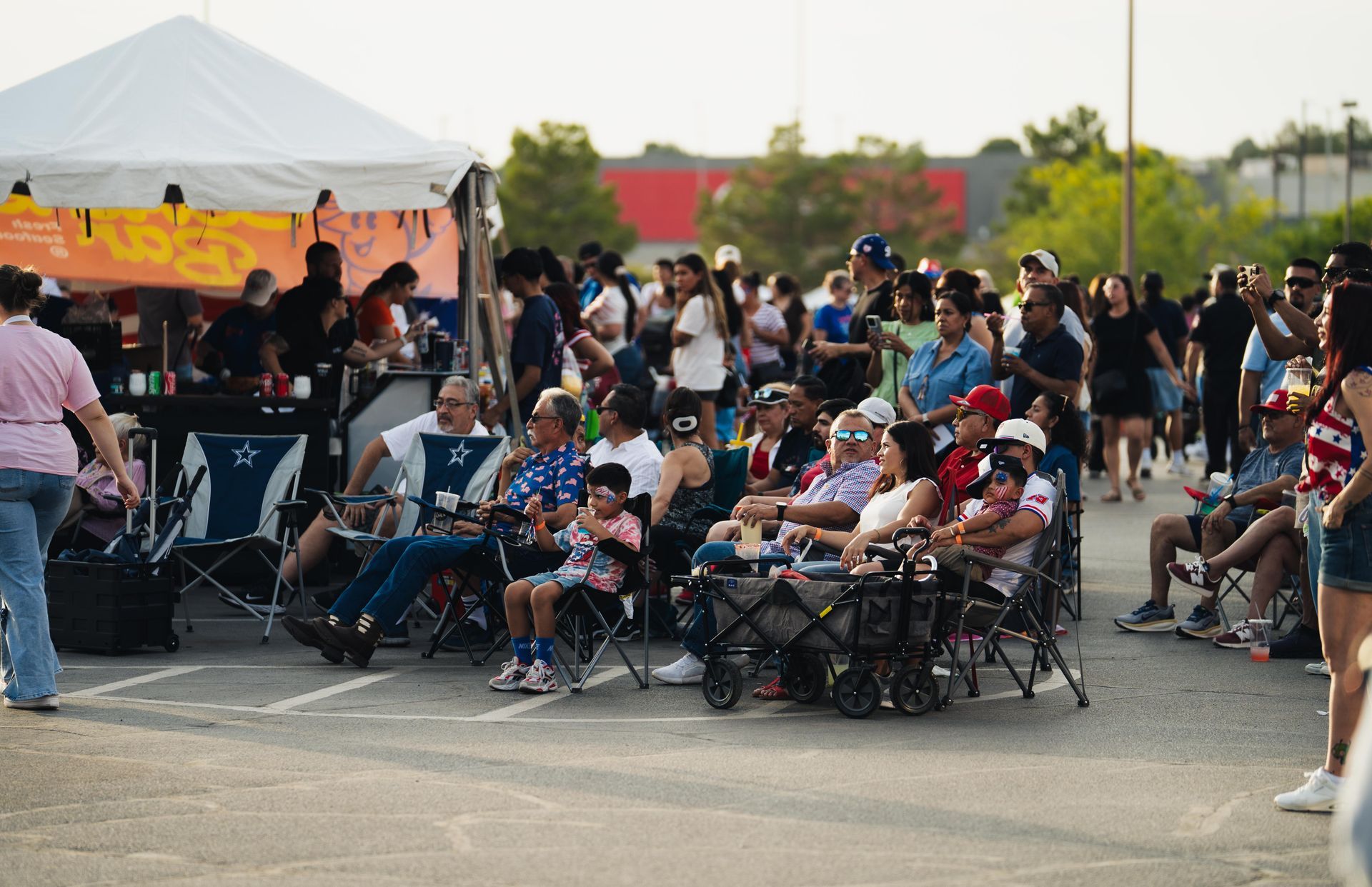 Crowd seated in folding chairs outdoors at a community event under a white tent