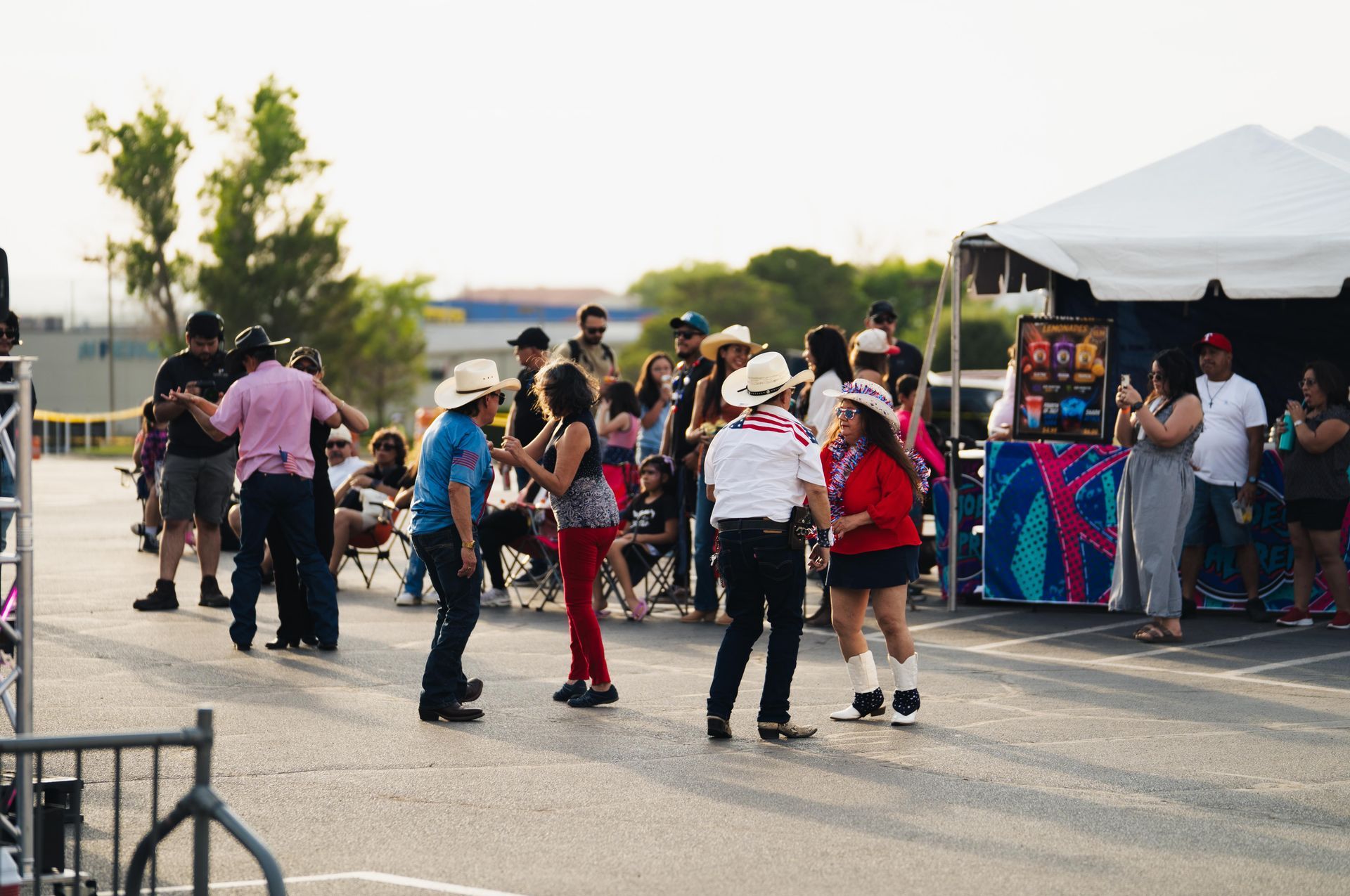 People gathered outdoors near a white tent, some dancing and watching music at a street festival.