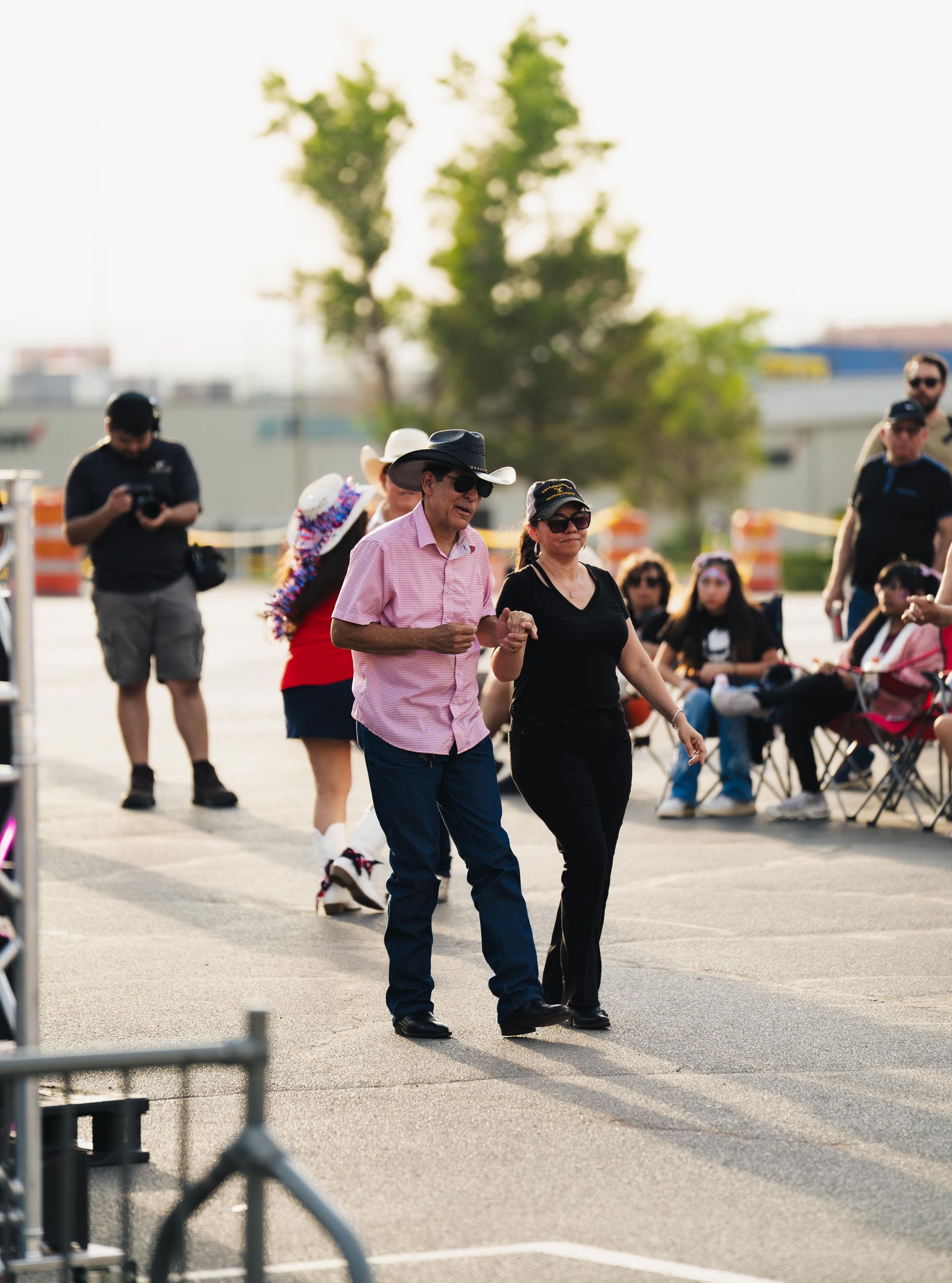 People dancing outdoors near seated spectators, with others standing in the background.