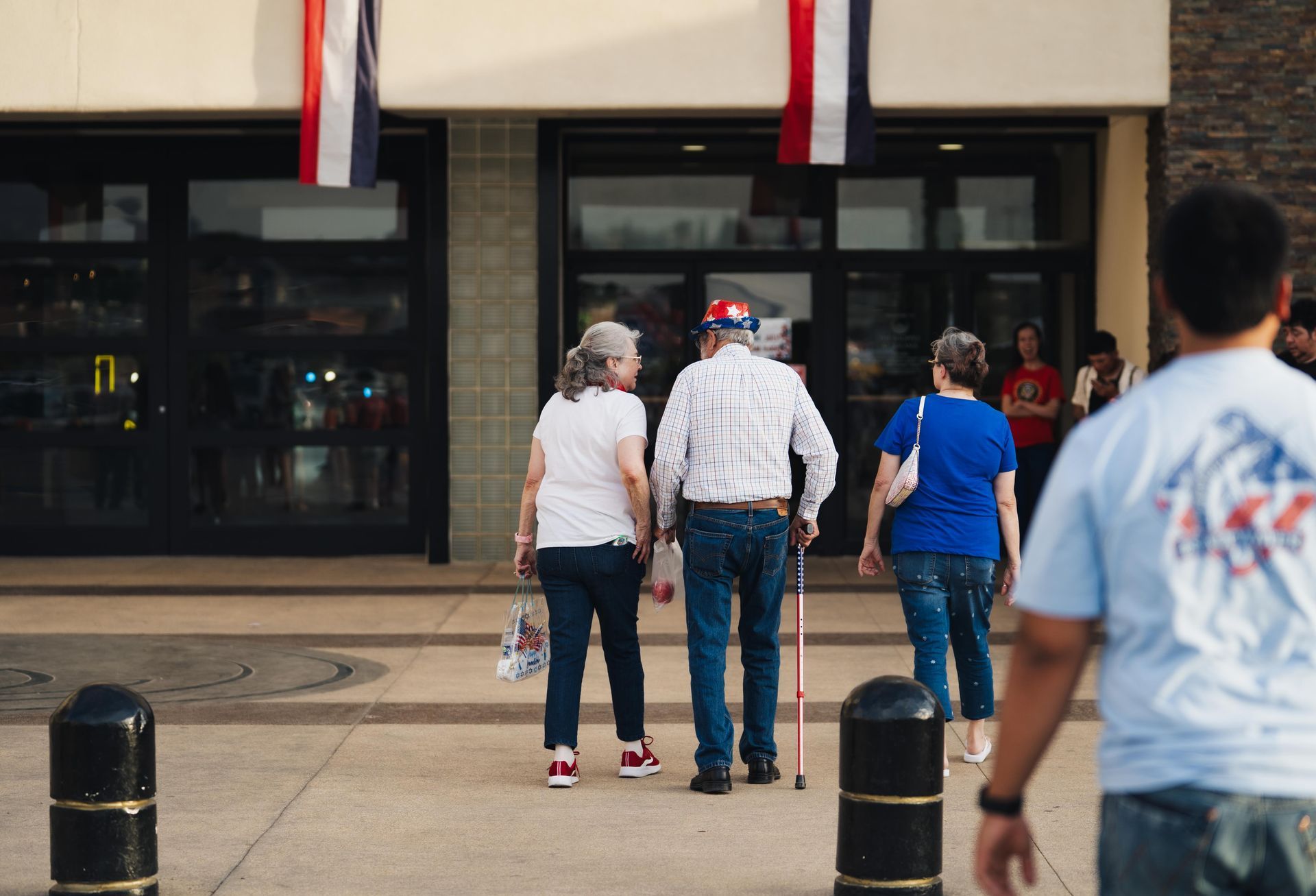 People walking toward a building entrance, with storefront windows and black bollards in front.
