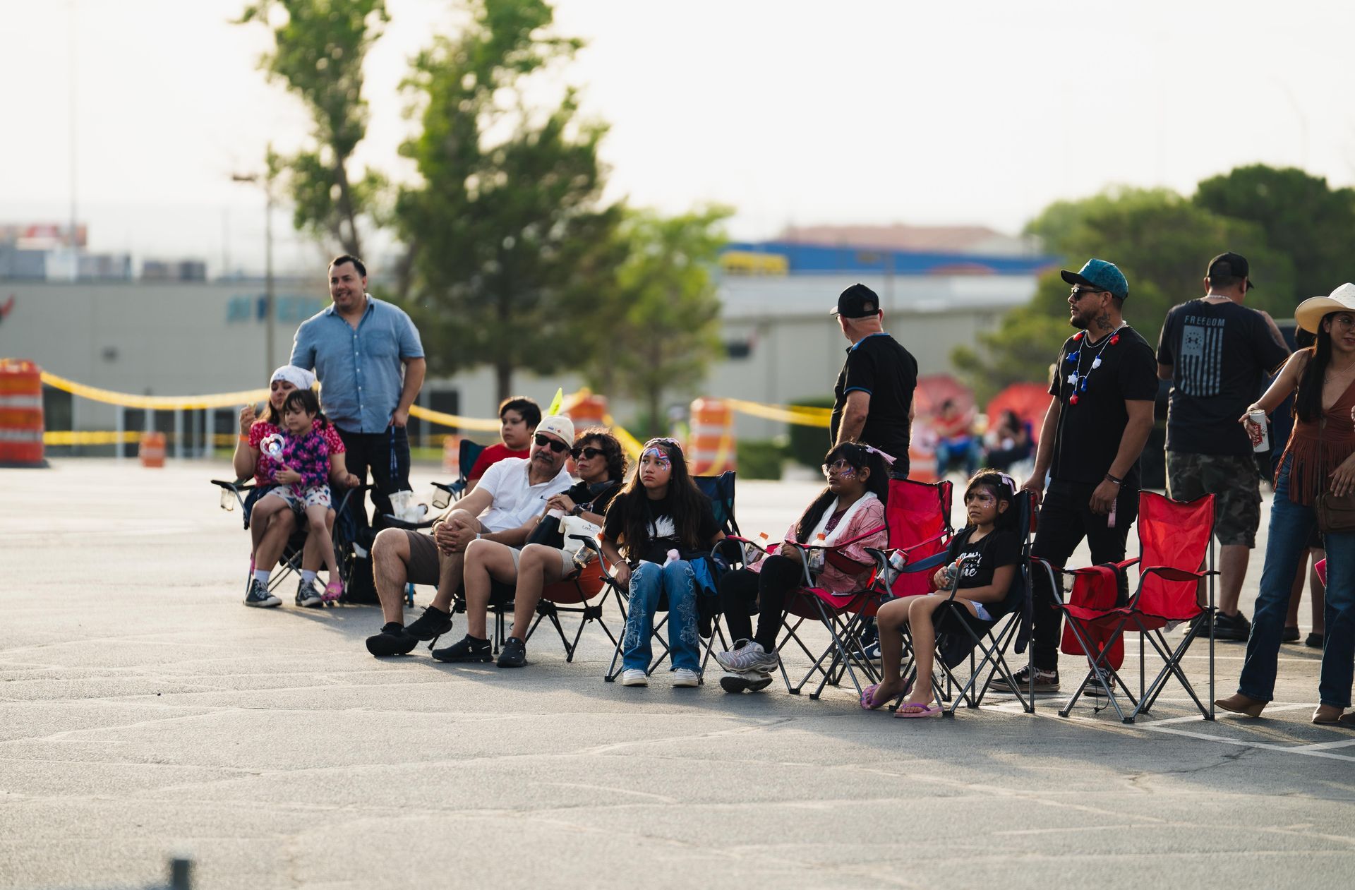 People seated in folding chairs along a road near orange barriers, waiting outdoors