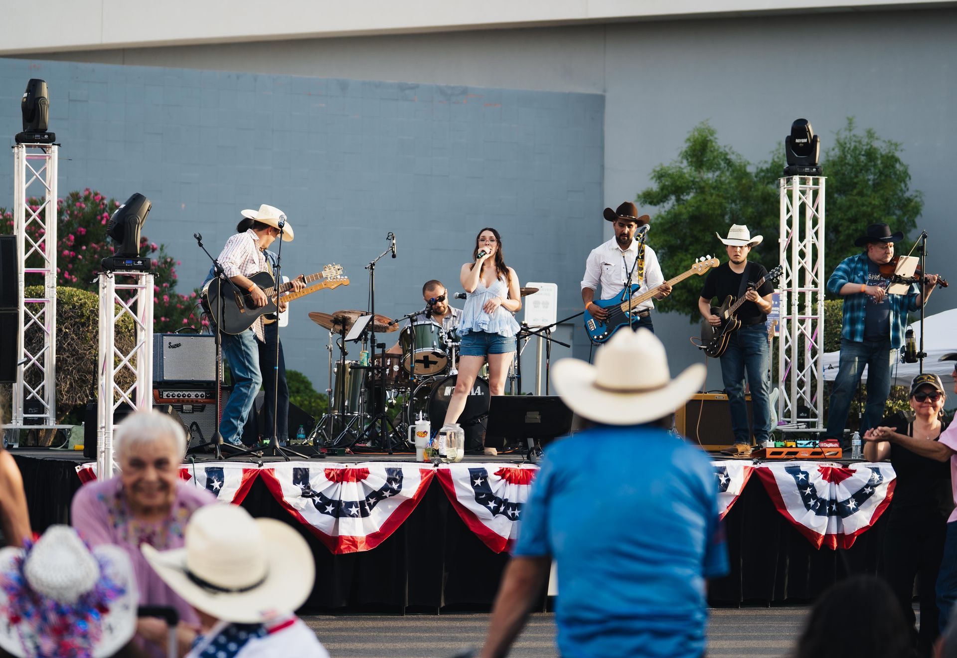Outdoor band performing on a stage decorated with red, white, and blue bunting, with audience in front