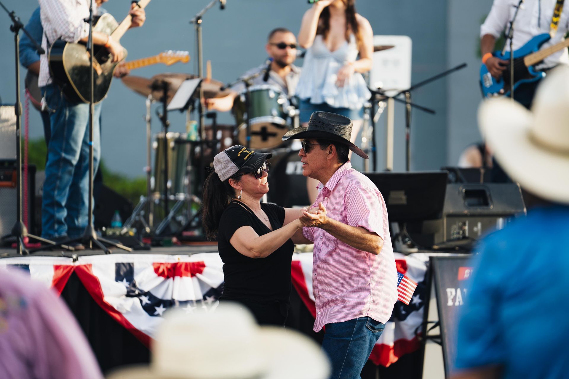 Couple dancing at an outdoor concert, with musicians performing on stage behind them