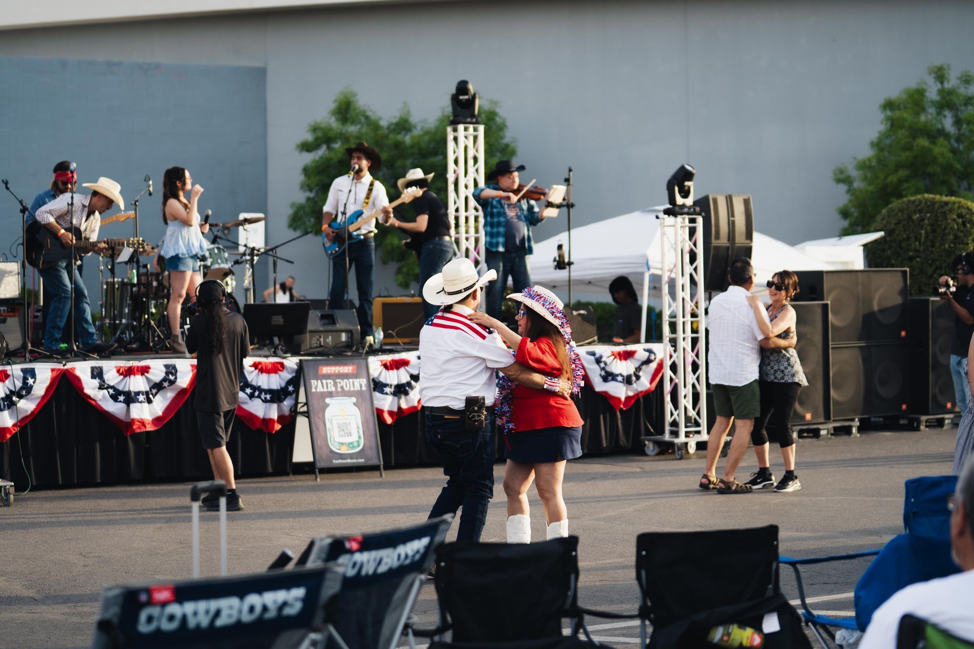 Outdoor concert with a band performing on a decorated stage and a couple dancing in front.
