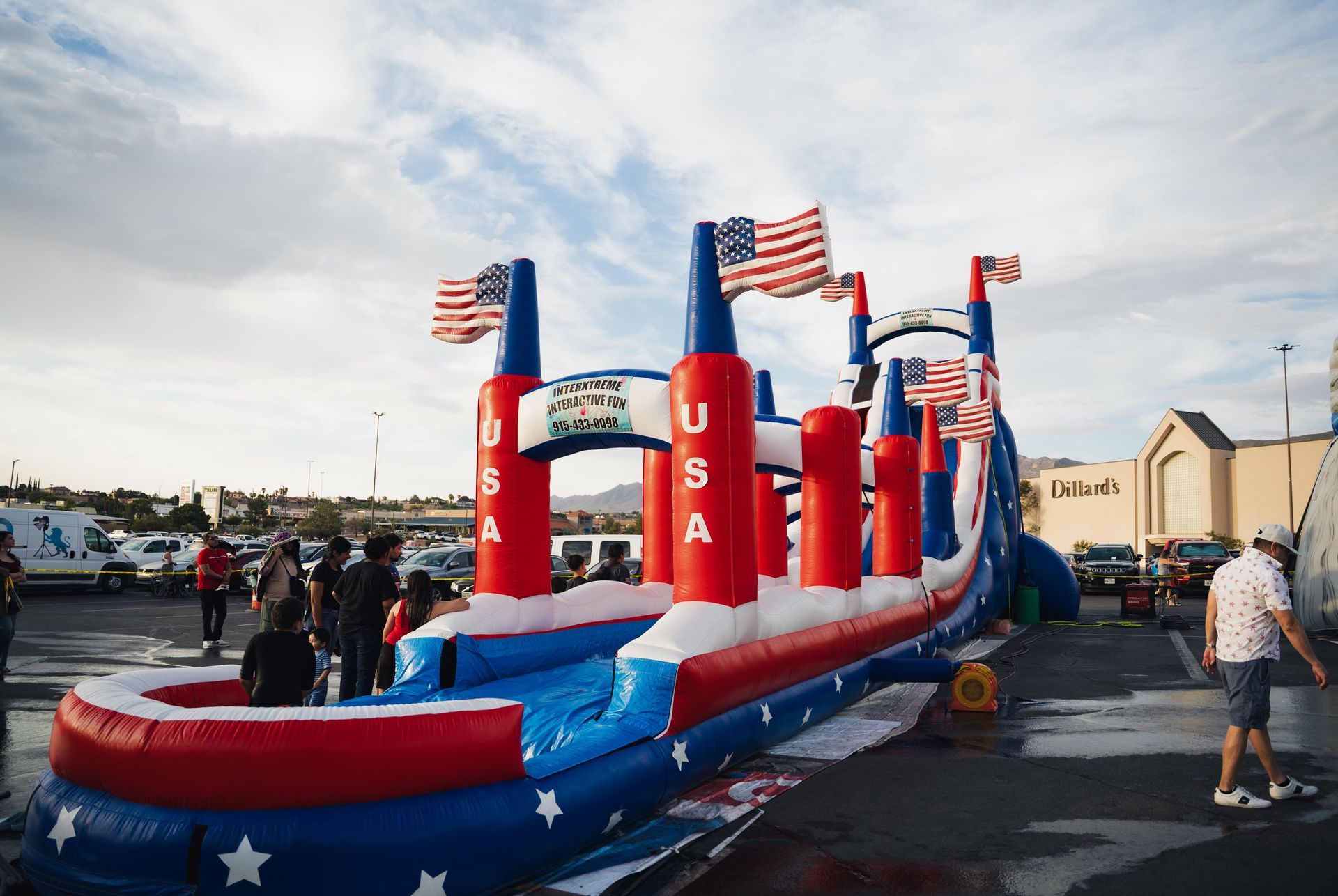 Red, white, and blue USA bounce house inflatable at an outdoor event with flags and people nearby
