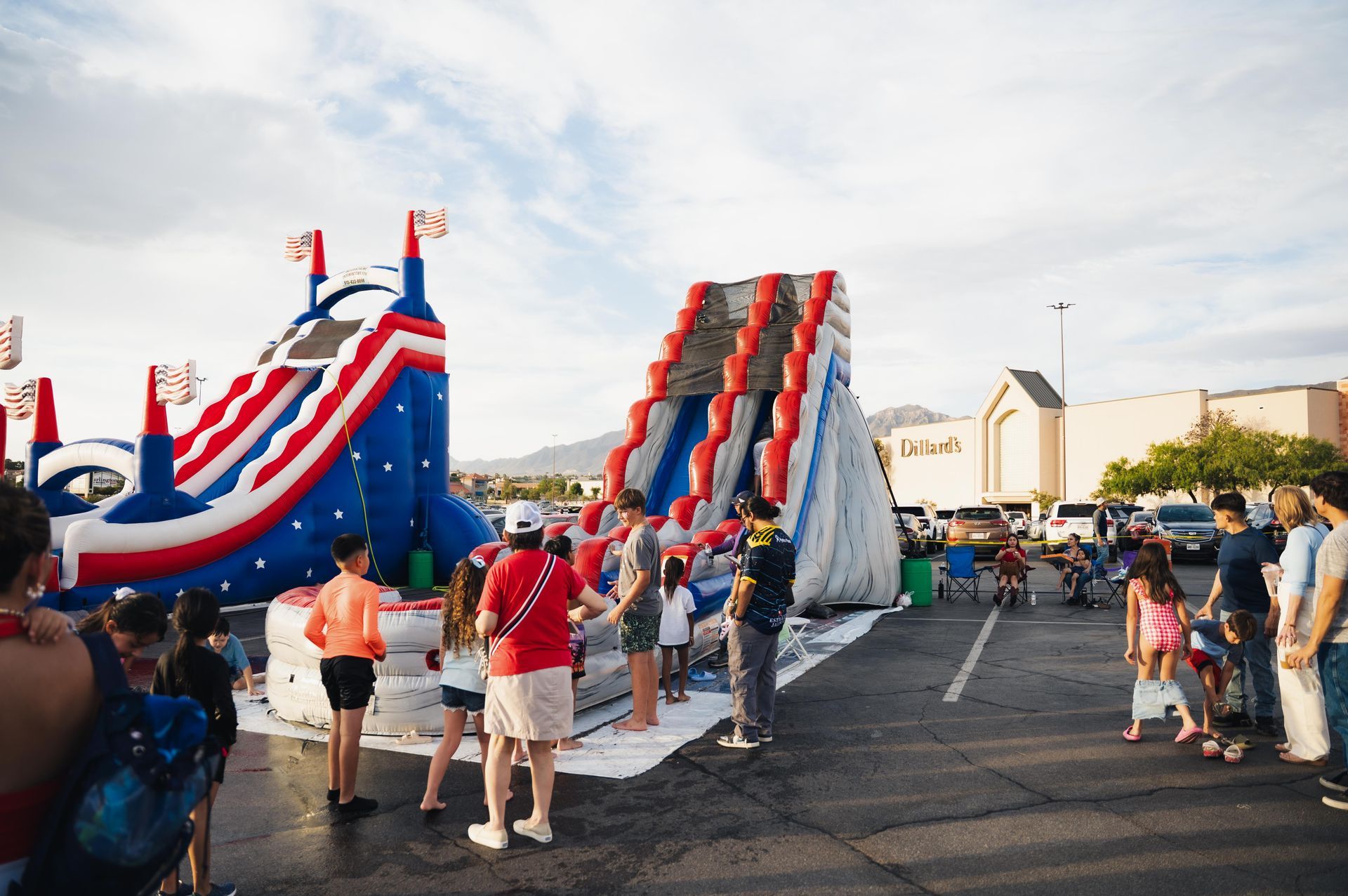 People gathered at a street event with large red, white, and blue inflatable slides.