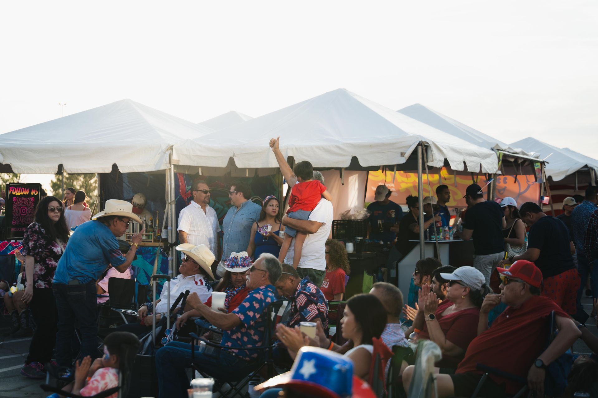 Crowd seated at an outdoor festival under white tents at sunset, with mountains in the background