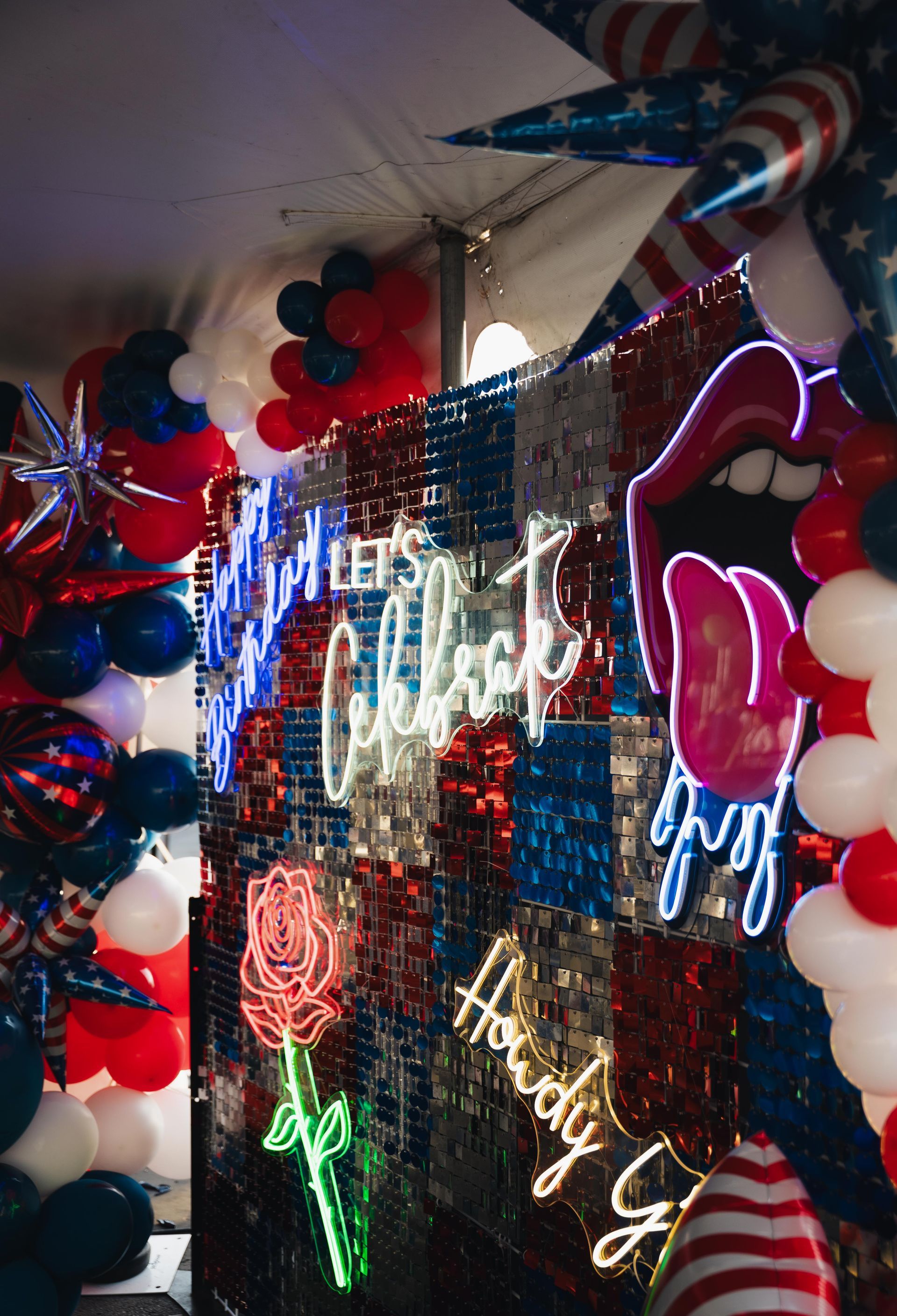 Neon-lit patriotic party wall with red, white, and blue balloons, stars, and glowing “Let’s celebrate” signs