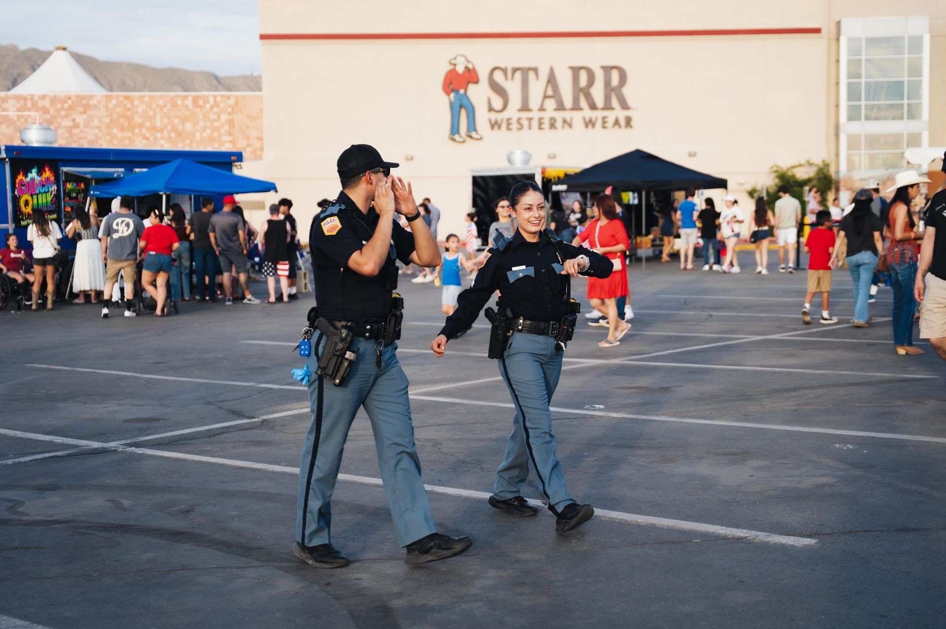 Two staff in black shirts stand in a parking lot outside Starr Western Wear, with a crowd in the background.