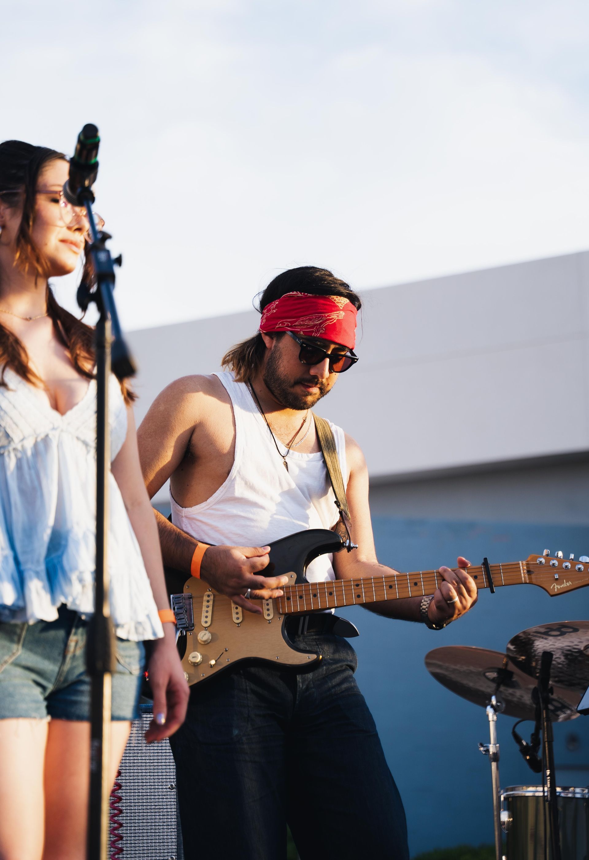 Musician in red bandana playing electric guitar beside a singer on an outdoor stage