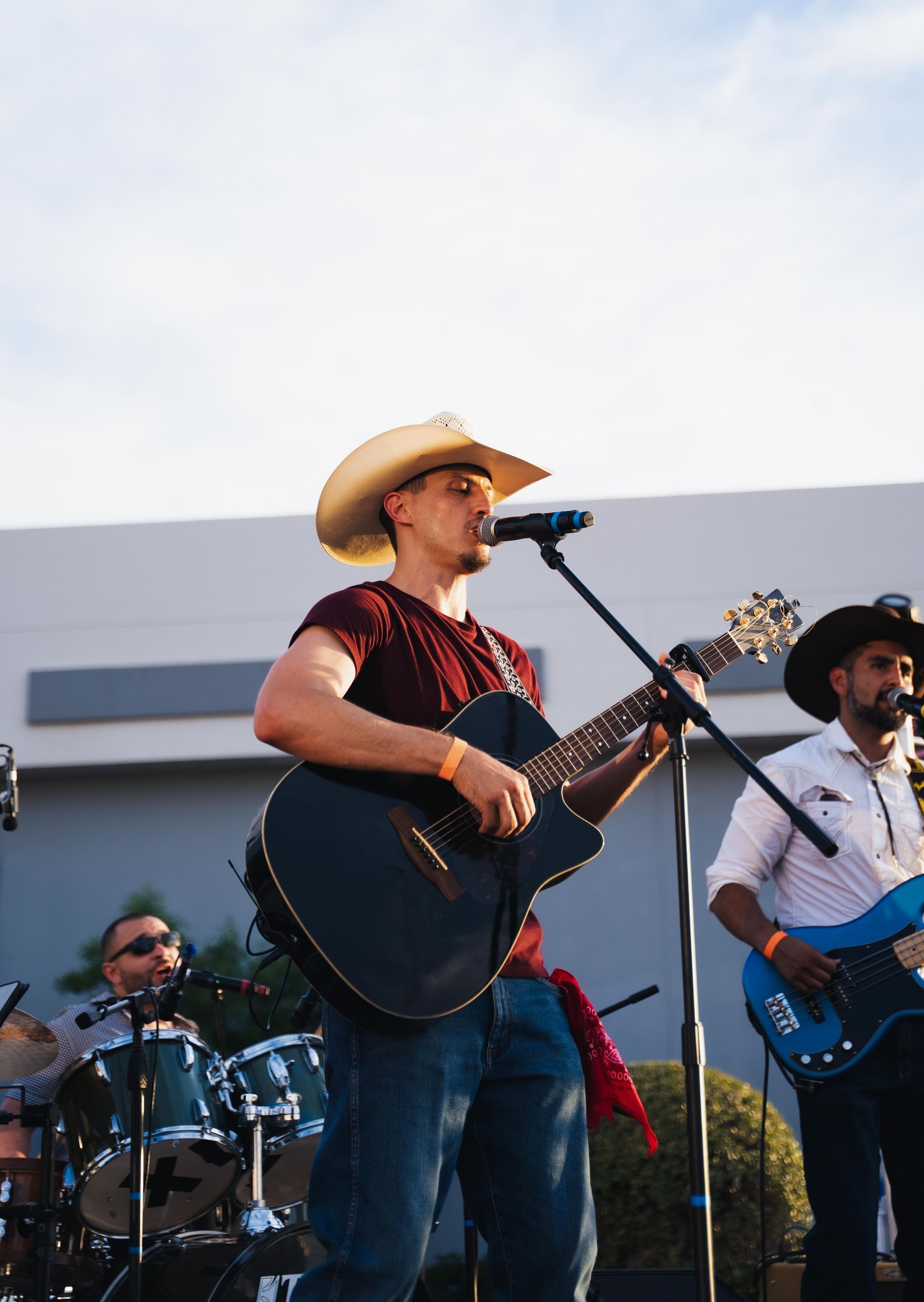 Country band performing outdoors, with a cowboy-hatted singer playing guitar at center stage.