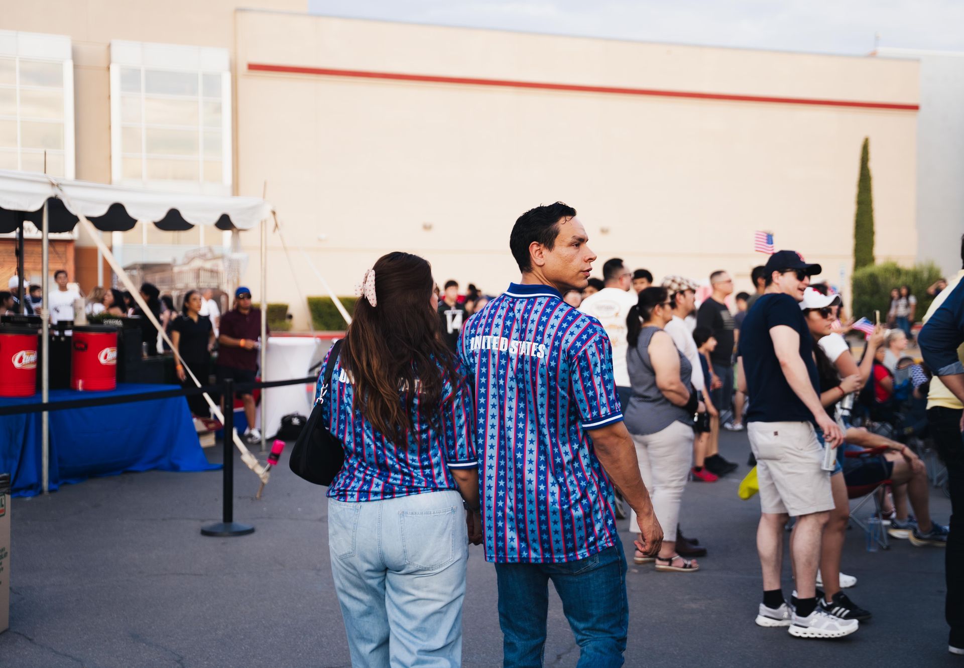 Crowd gathered outdoors near a booth, with two people in blue plaid shirts in the foreground