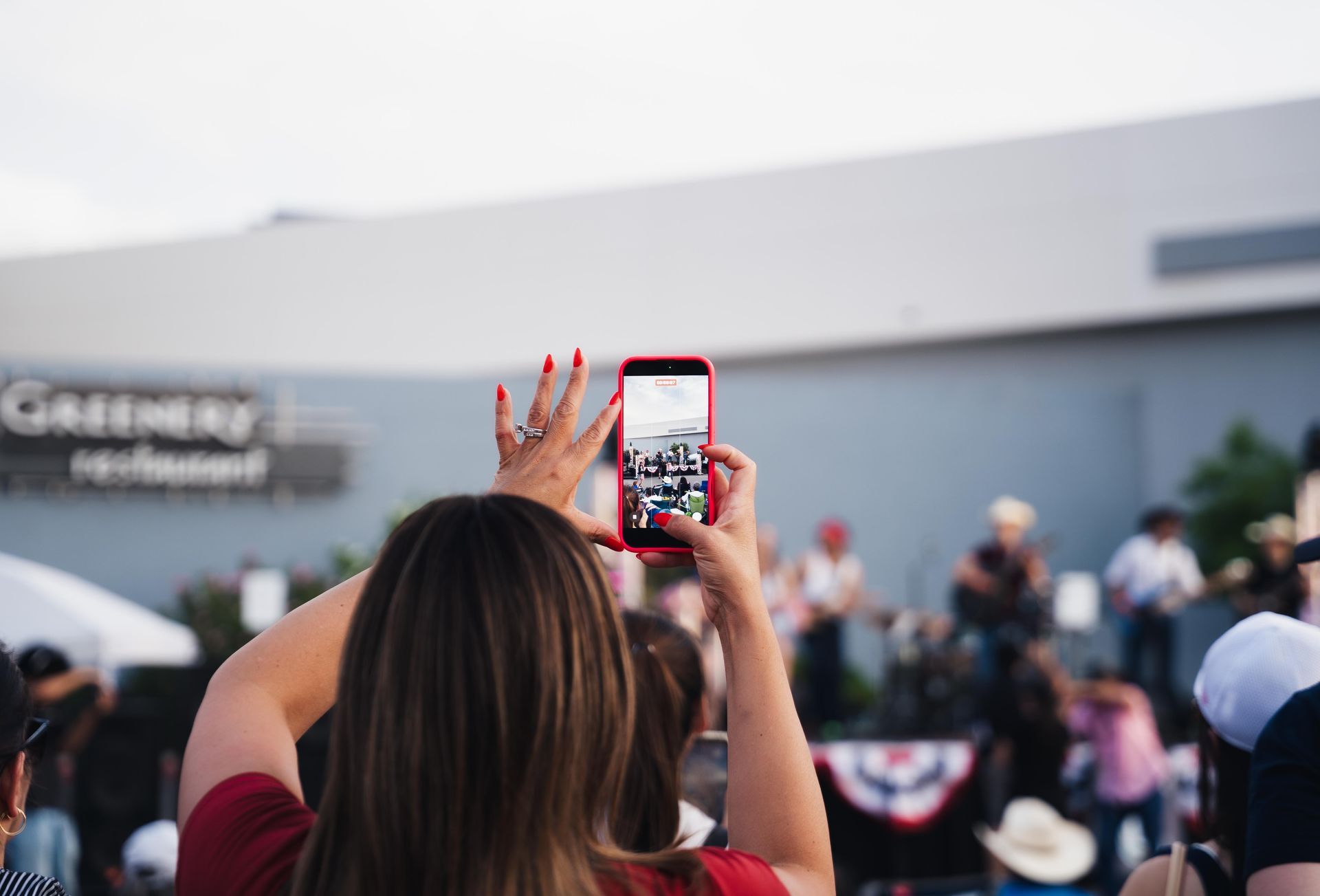 Person holds up a smartphone to record a crowd at an outdoor event near a building
