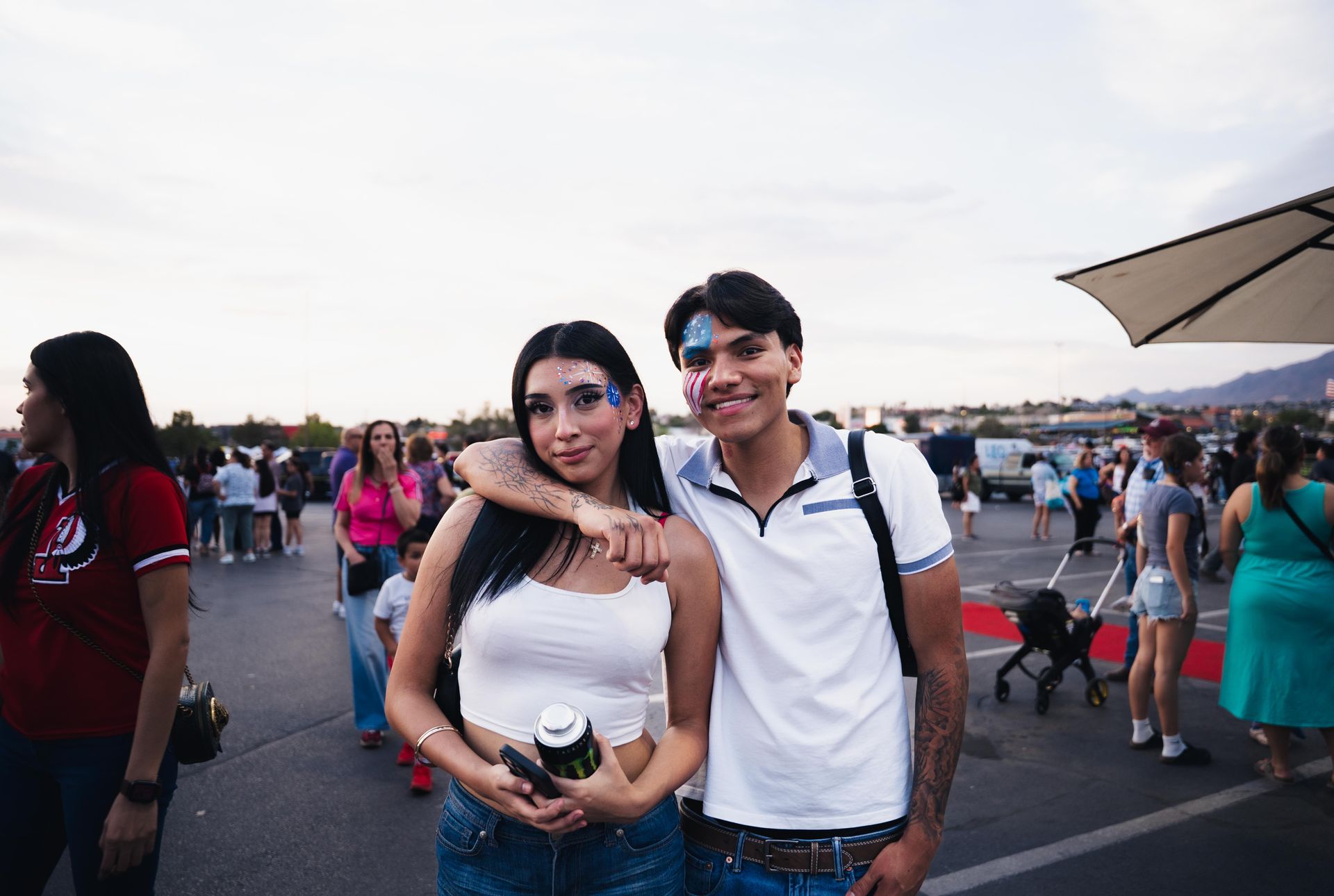 Two people smiling and posing at an outdoor event, with a crowd in the background.
