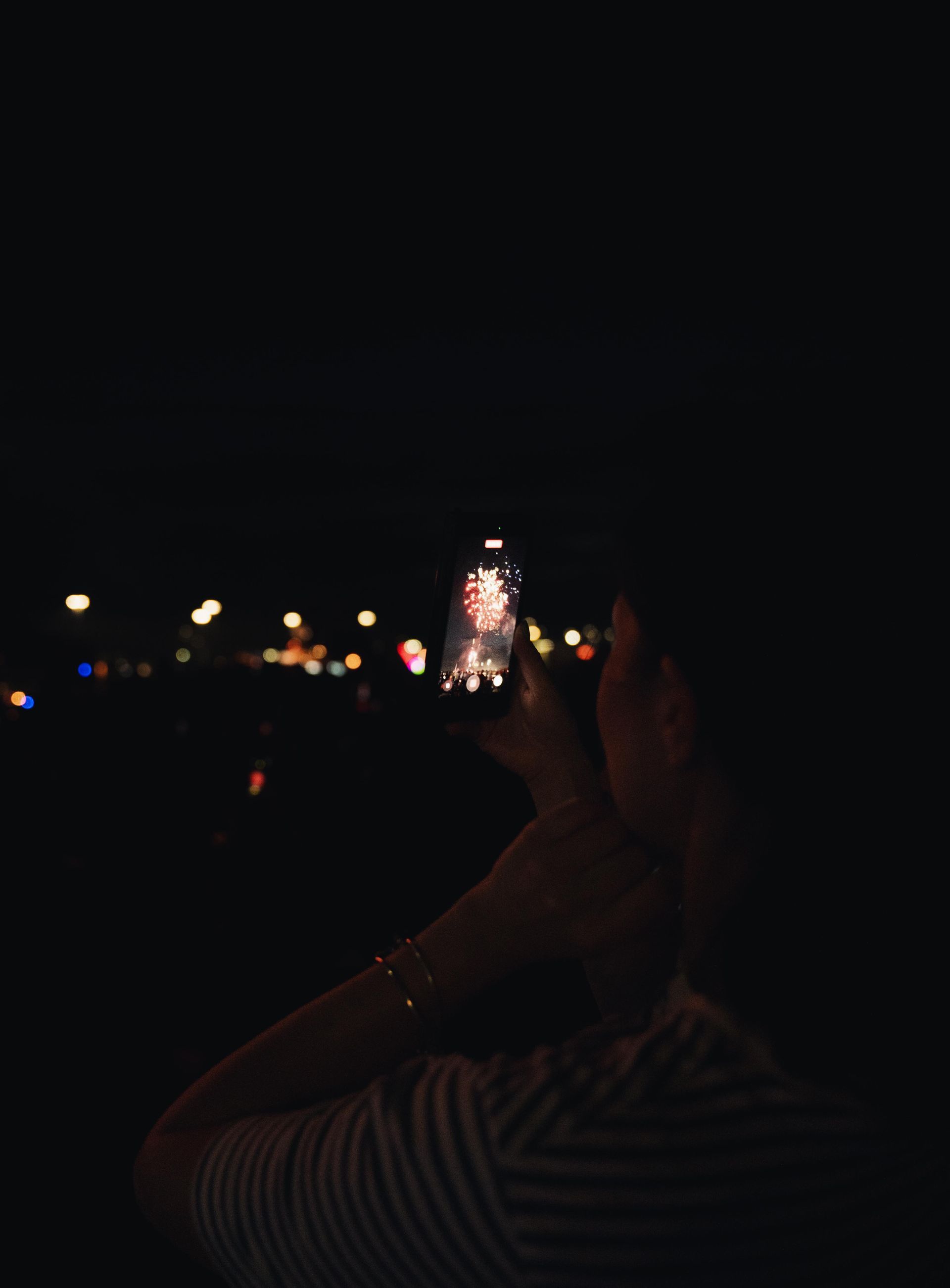 Dark outdoor crowd scene with blurred lights and a hand raised in the foreground.