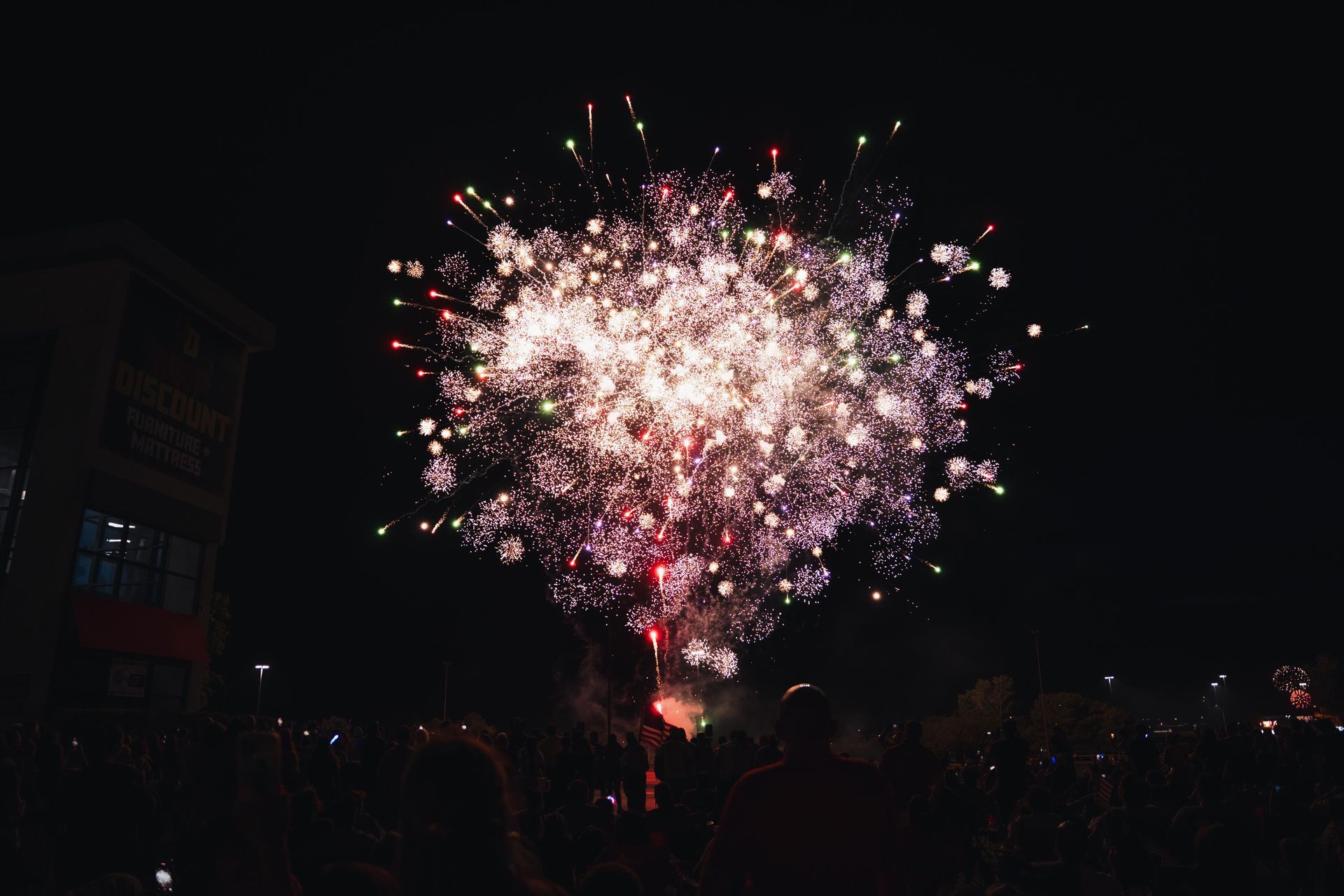 Bright pink and white fireworks burst over a dark city skyline at night