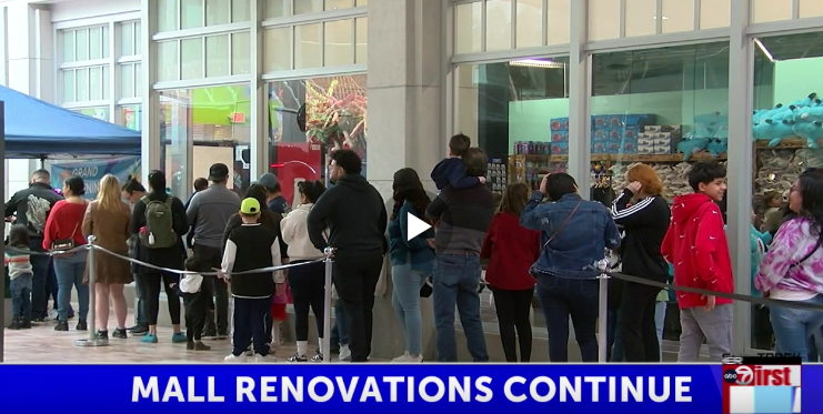 People waiting outside a mall entrance during renovations, with workers and barriers visible.