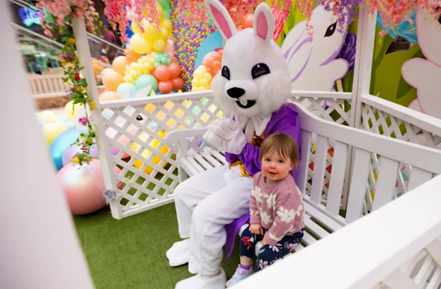 Child sitting with a white bunny mascot in a colorful party play area
