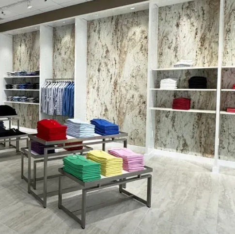 Modern clothing store with folded shirts on tables, hanging clothes, and marble-patterned walls