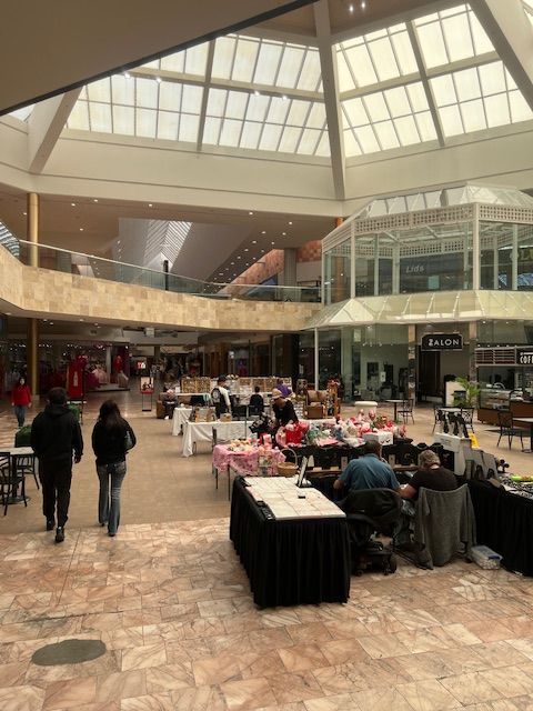Indoor shopping mall atrium with skylight, tables, and a few people walking and sitting nearby