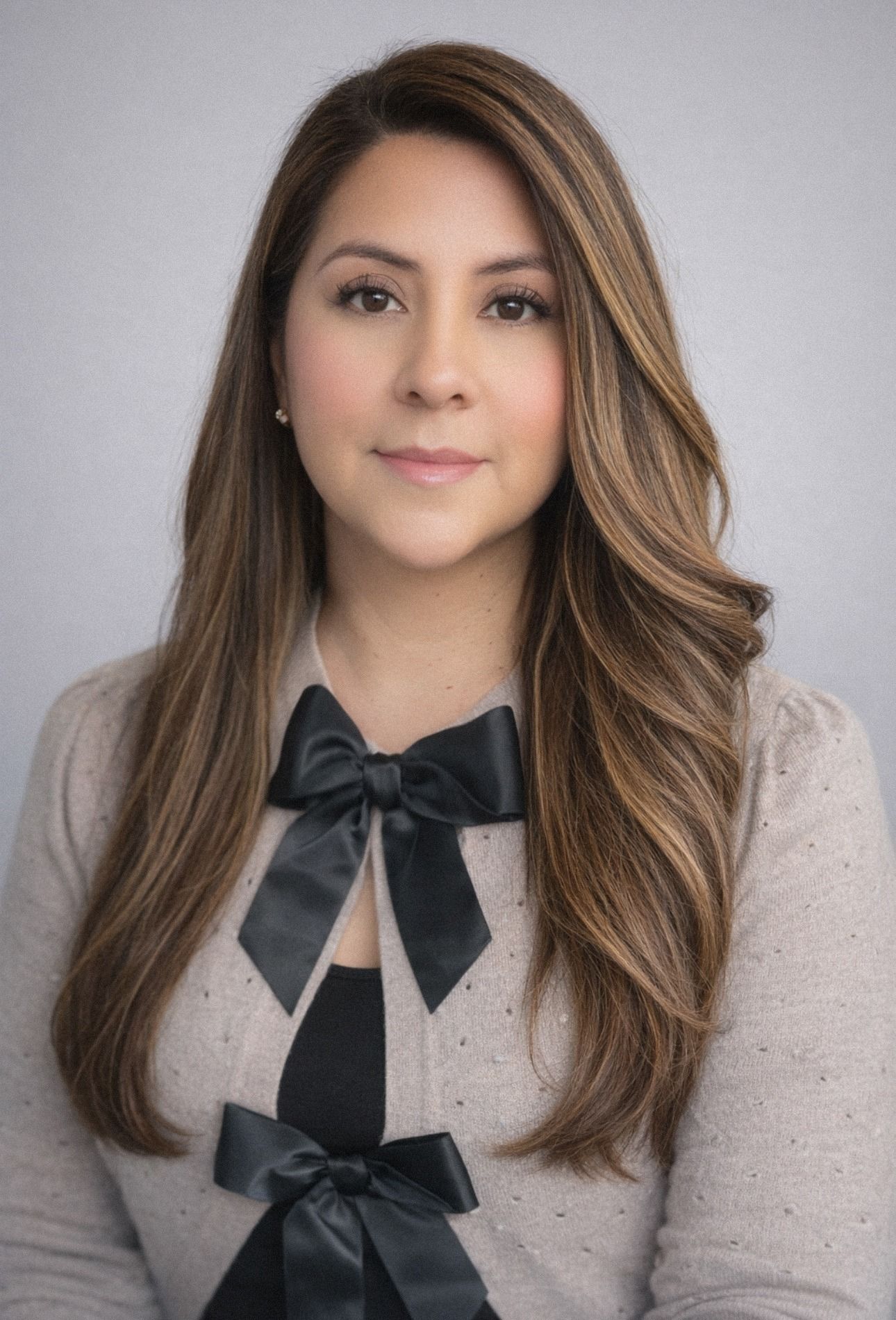 Woman in a beige sweater with black bows, posed against a gray background.