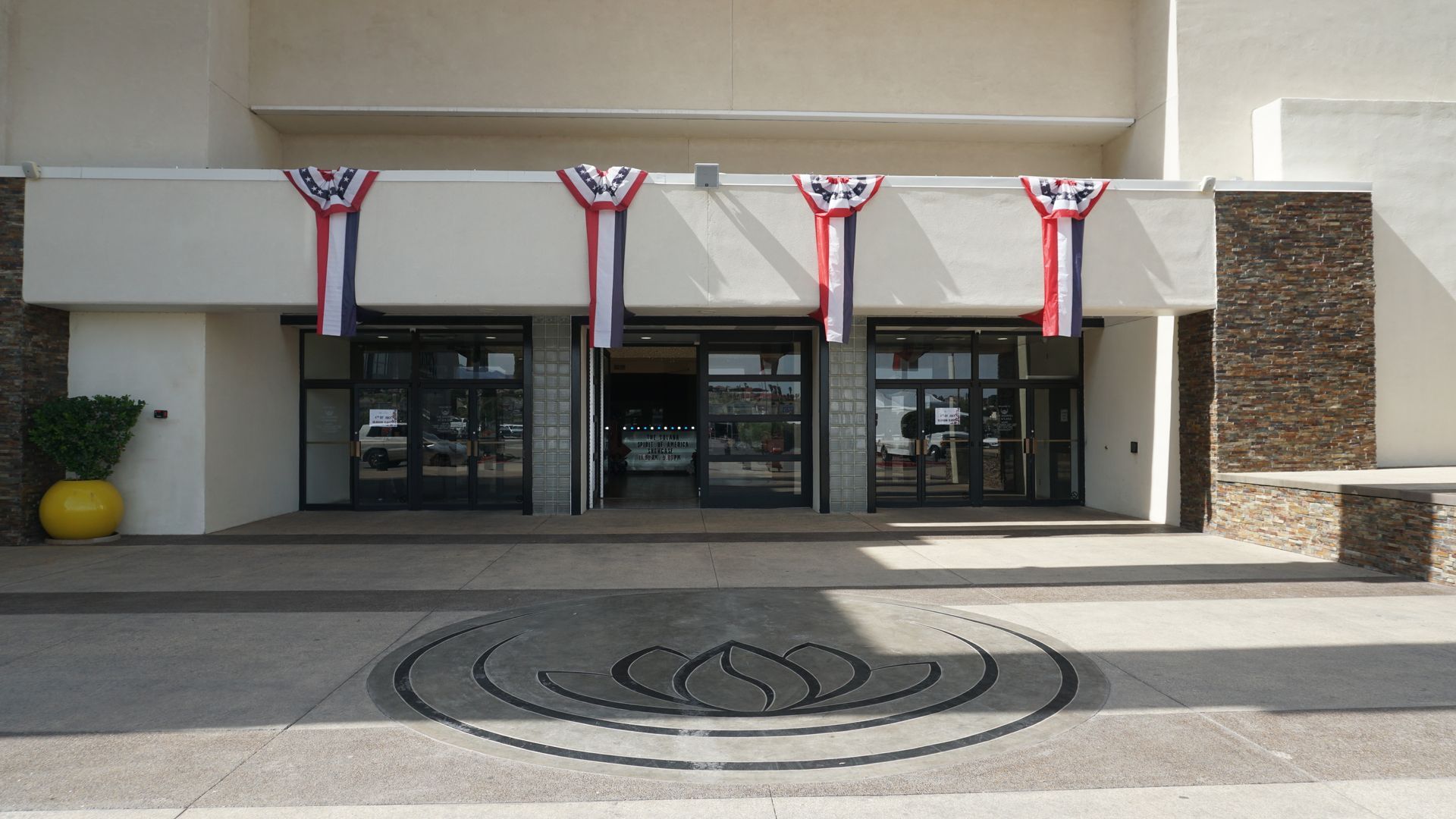 Building entrance decorated with red, white, and blue bunting above glass doors, with a circular emblem in the pavement.